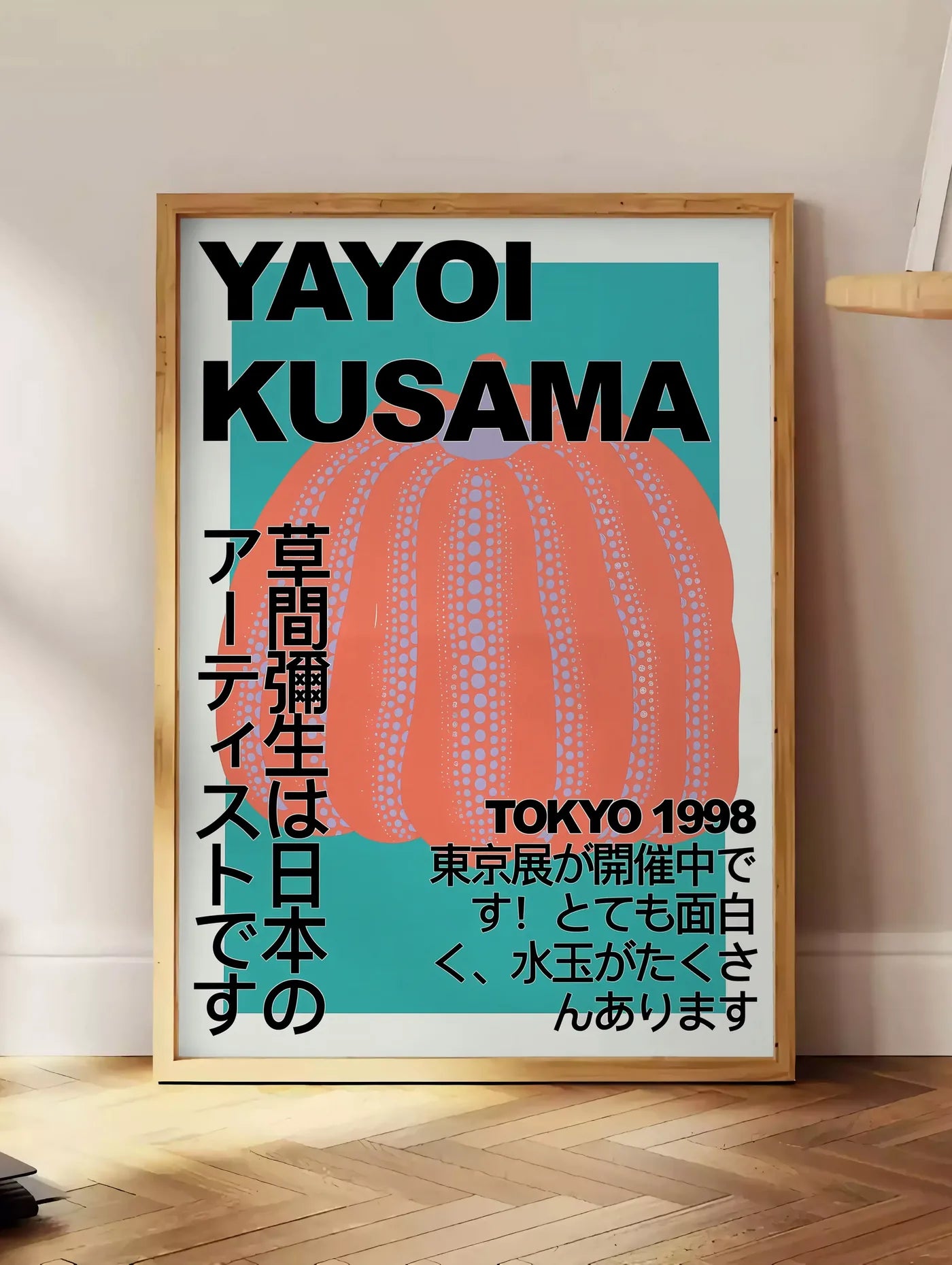 Estampe affiche citrouille orange de Kusama art japonais, posee au sol dans un coin salon, sur un parquet a chevrons, pres d'une table d'appoint en chene chargee de livres