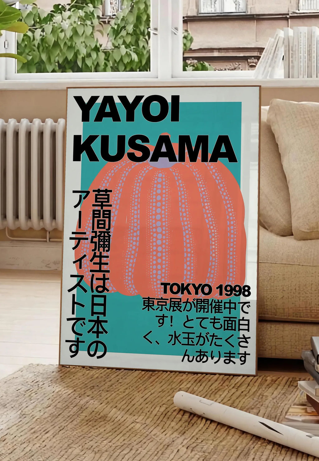 Poster affiche citrouille orange de Kusama art japonais, posee au sol dans un salon parisien, devant une grande fenetre donnant sur un immeuble haussmannien, entre un ficus et un canape creme
