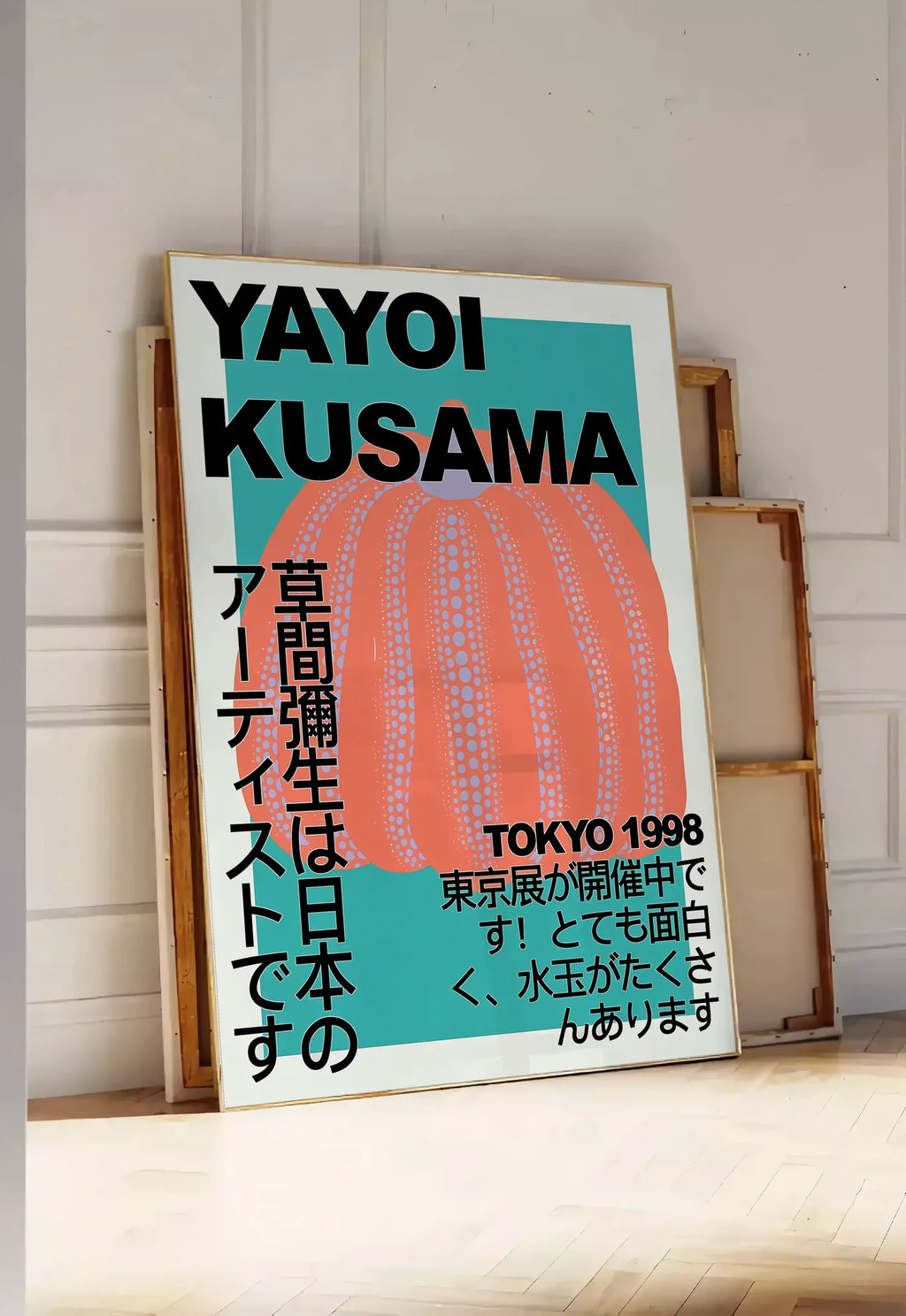 Tirage encadrable affiche citrouille orange de Kusama art japonais, posee au sol dans une entree lumineuse, contre un mur a panneaux blancs, a cote de chassis en bois empiles