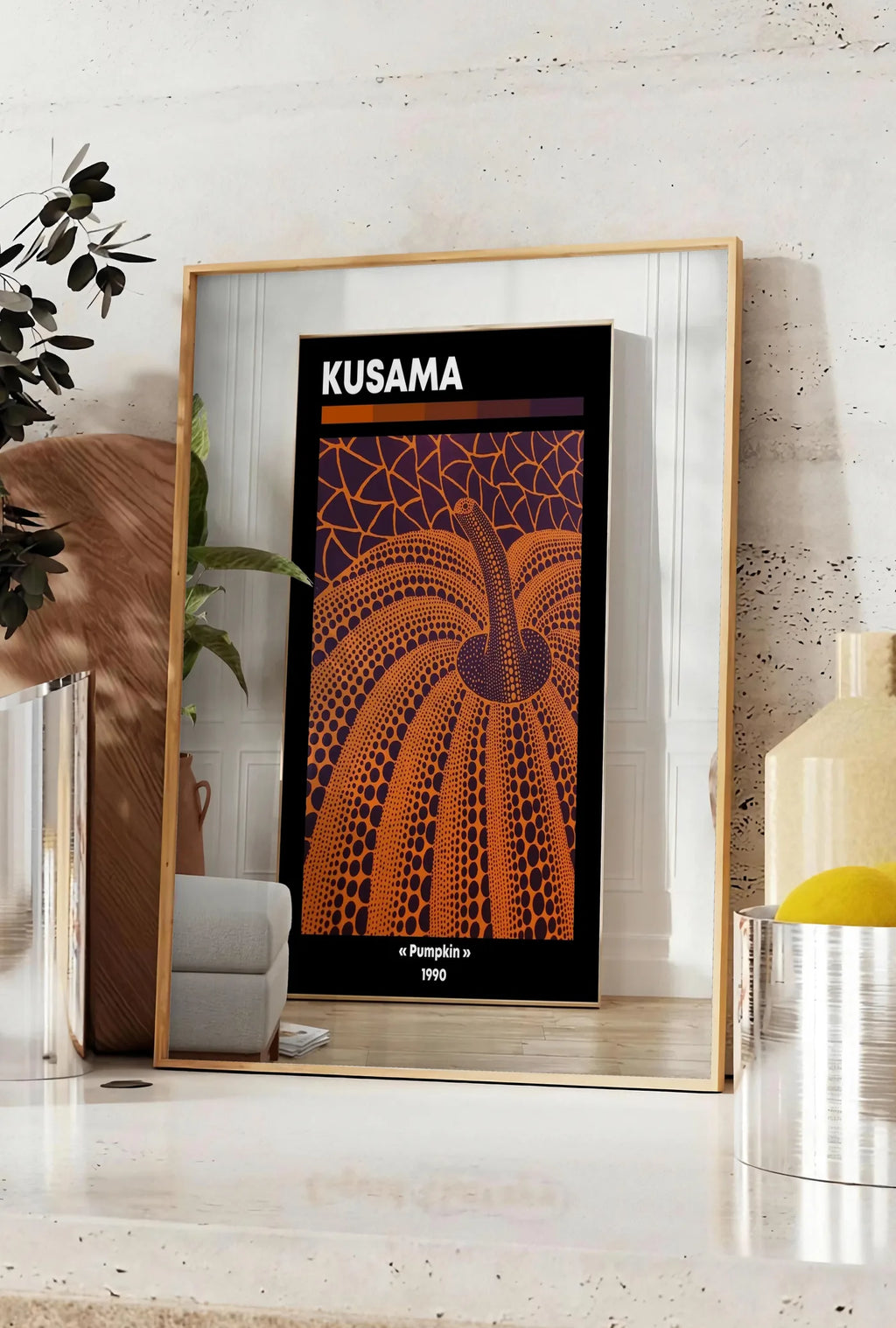Affiche affiche Kusama citrouille orange a pois sur fond violet, posee sur un plan de travail de cuisine en pierre claire, entre une branche d'eucalyptus en vase et un bocal de citrons