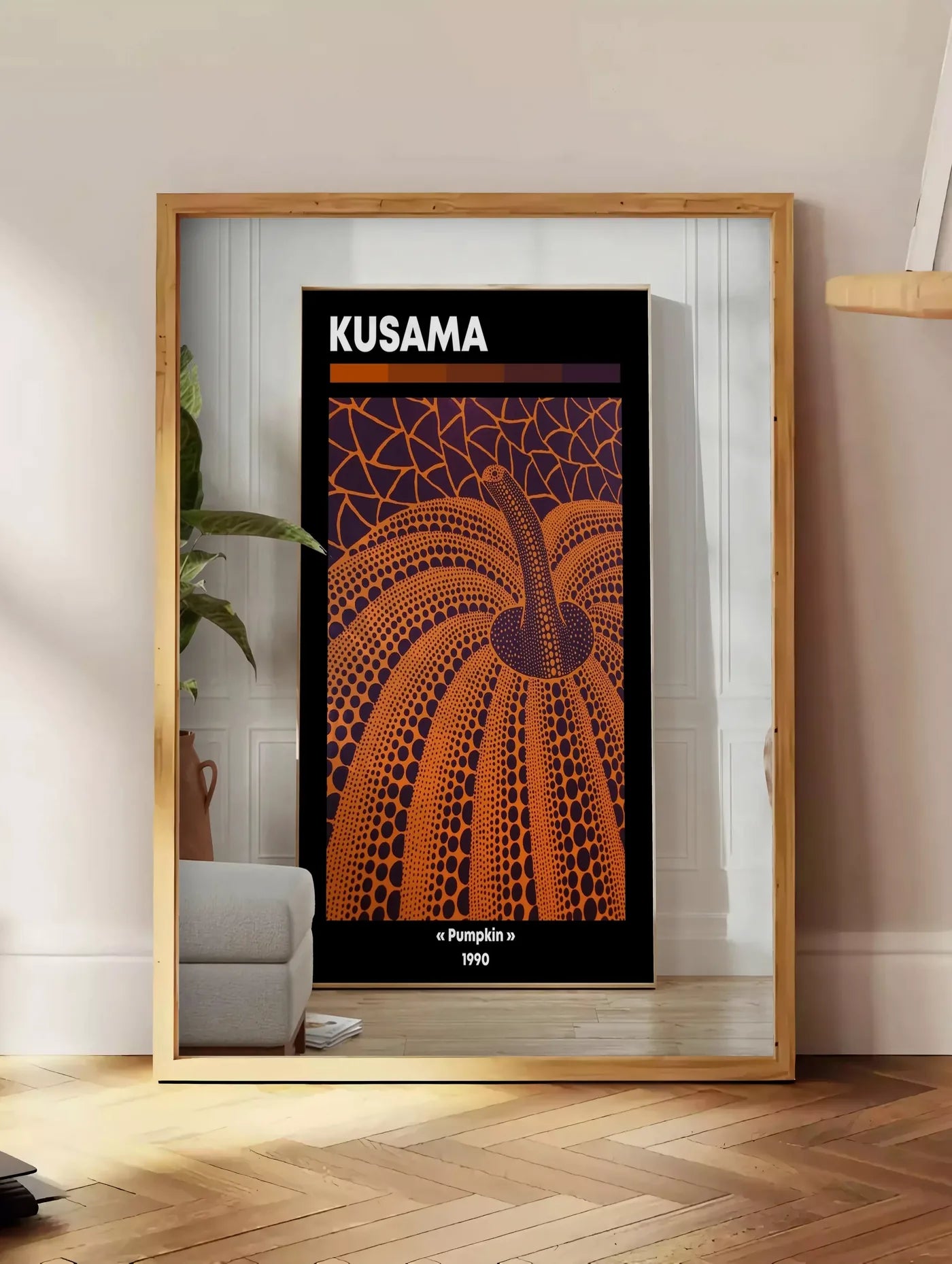 Estampe affiche Kusama citrouille orange a pois sur fond violet, posee au sol dans un coin salon, sur un parquet a chevrons, pres d'une table d'appoint en chene chargee de livres