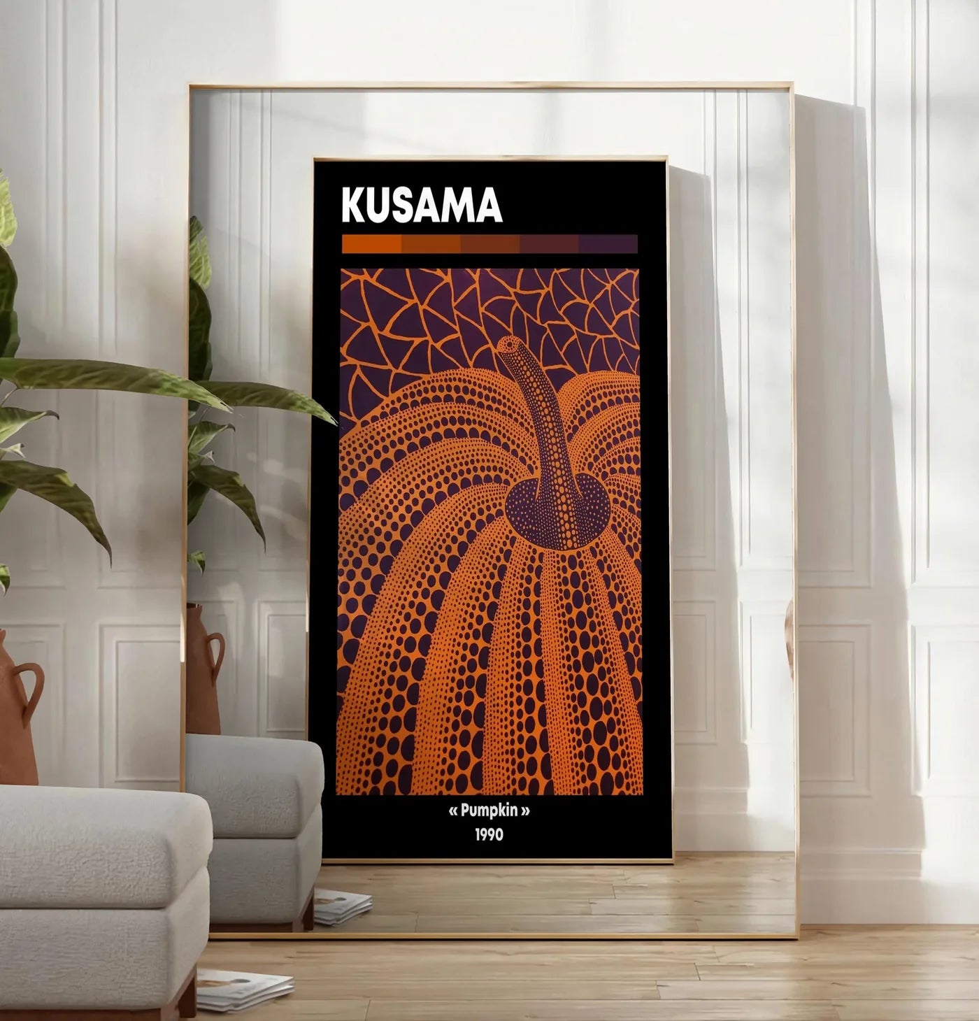 Reproduction affiche Kusama citrouille orange a pois sur fond violet, posee au sol dans un salon minimaliste clair, a cote d'un canape beige et d'une plante verte, sur un parquet clair