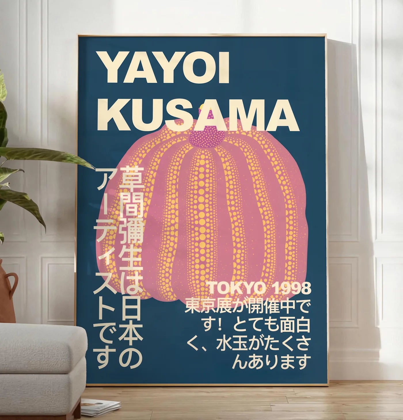 Reproduction affiche Kusama citrouille rose a pois sur fond bleu nuit, posee au sol dans un salon minimaliste clair, a cote d'un canape beige et d'une plante verte, sur un parquet clair