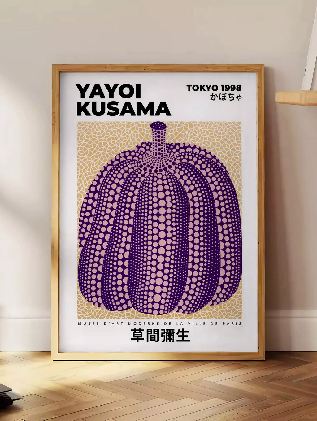 Estampe affiche Kusama citrouille violette a pois sur fond beige, posee au sol dans un coin salon, sur un parquet a chevrons, pres d'une table d'appoint en chene chargee de livres