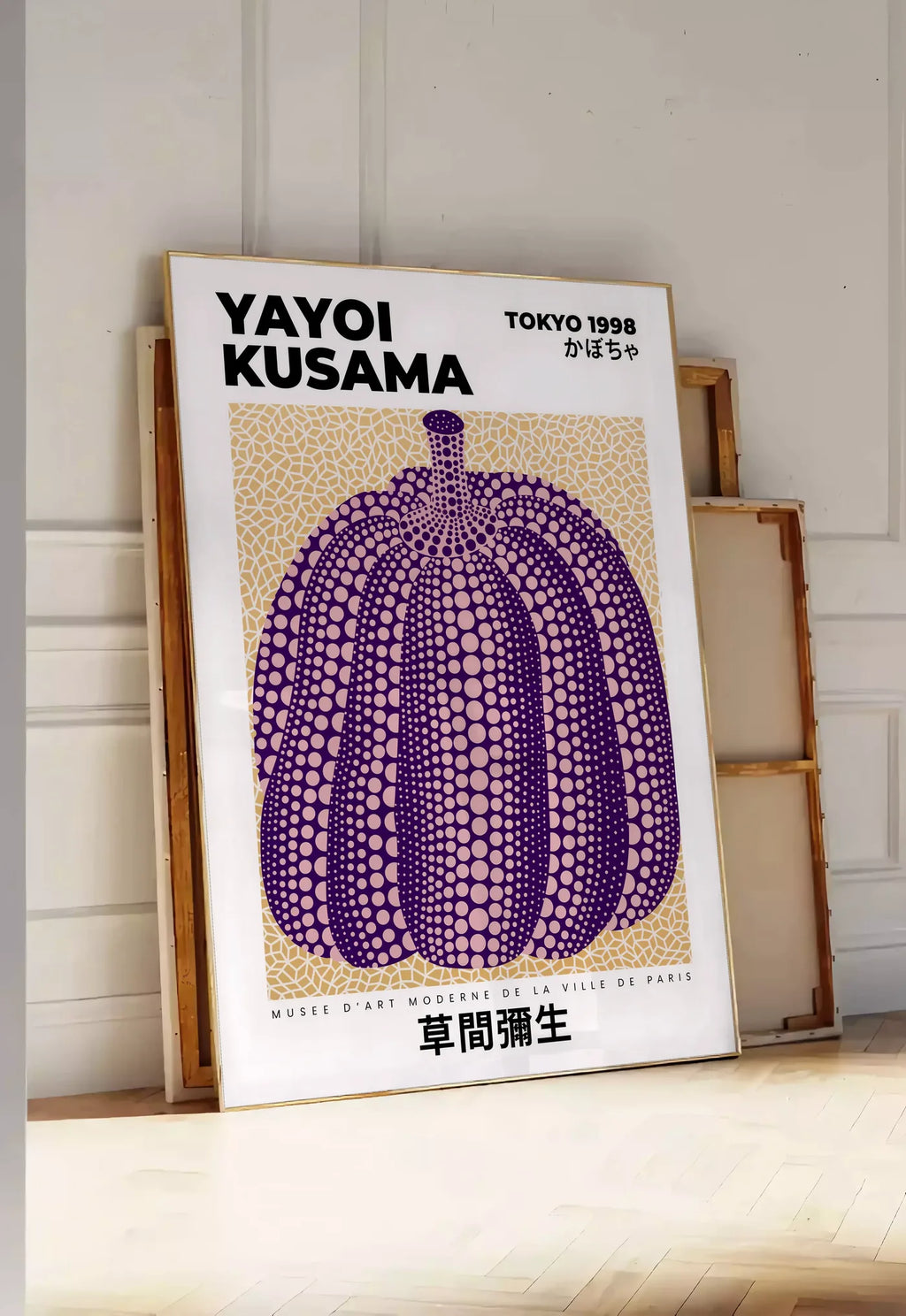 Tirage encadrable affiche Kusama citrouille violette a pois sur fond beige, posee au sol dans une entree lumineuse, contre un mur a panneaux blancs, a cote de chassis en bois empiles