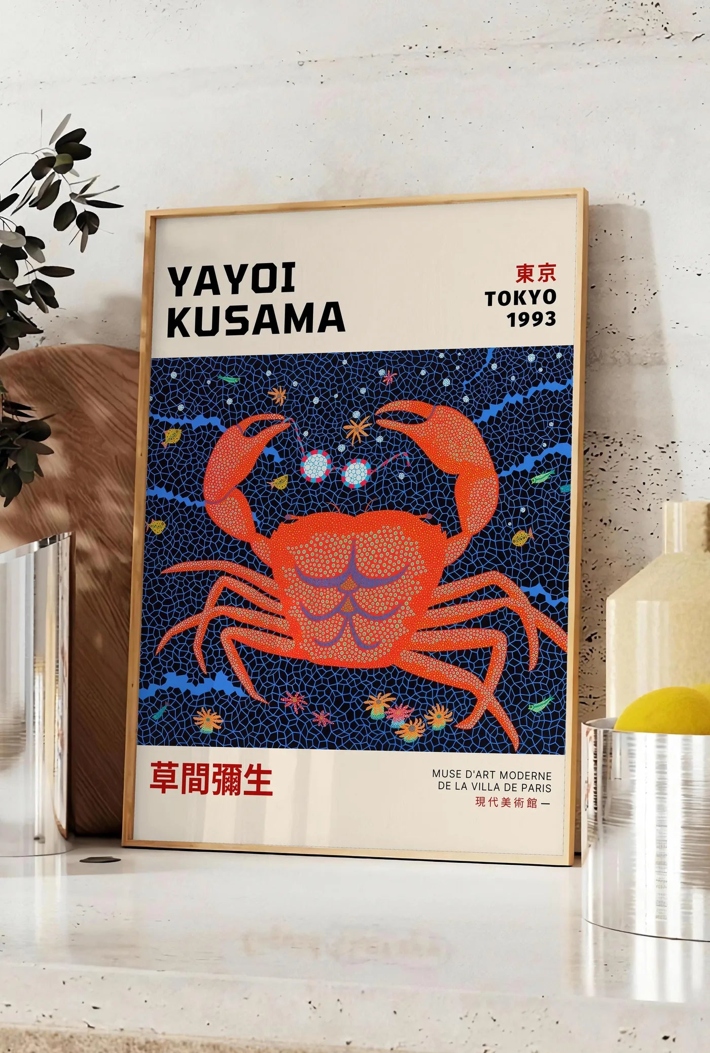 Affiche affiche crabe rouge a pois de Kusama art japonais, posee sur un plan de travail de cuisine en pierre claire, entre une branche d'eucalyptus en vase et un bocal de citrons