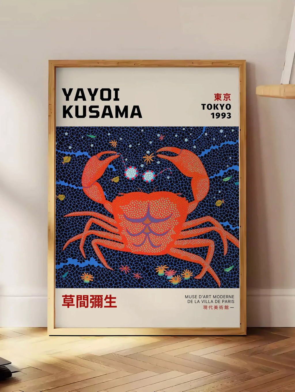 Estampe affiche crabe rouge a pois de Kusama art japonais, posee au sol dans un coin salon, sur un parquet a chevrons, pres d'une table d'appoint en chene chargee de livres