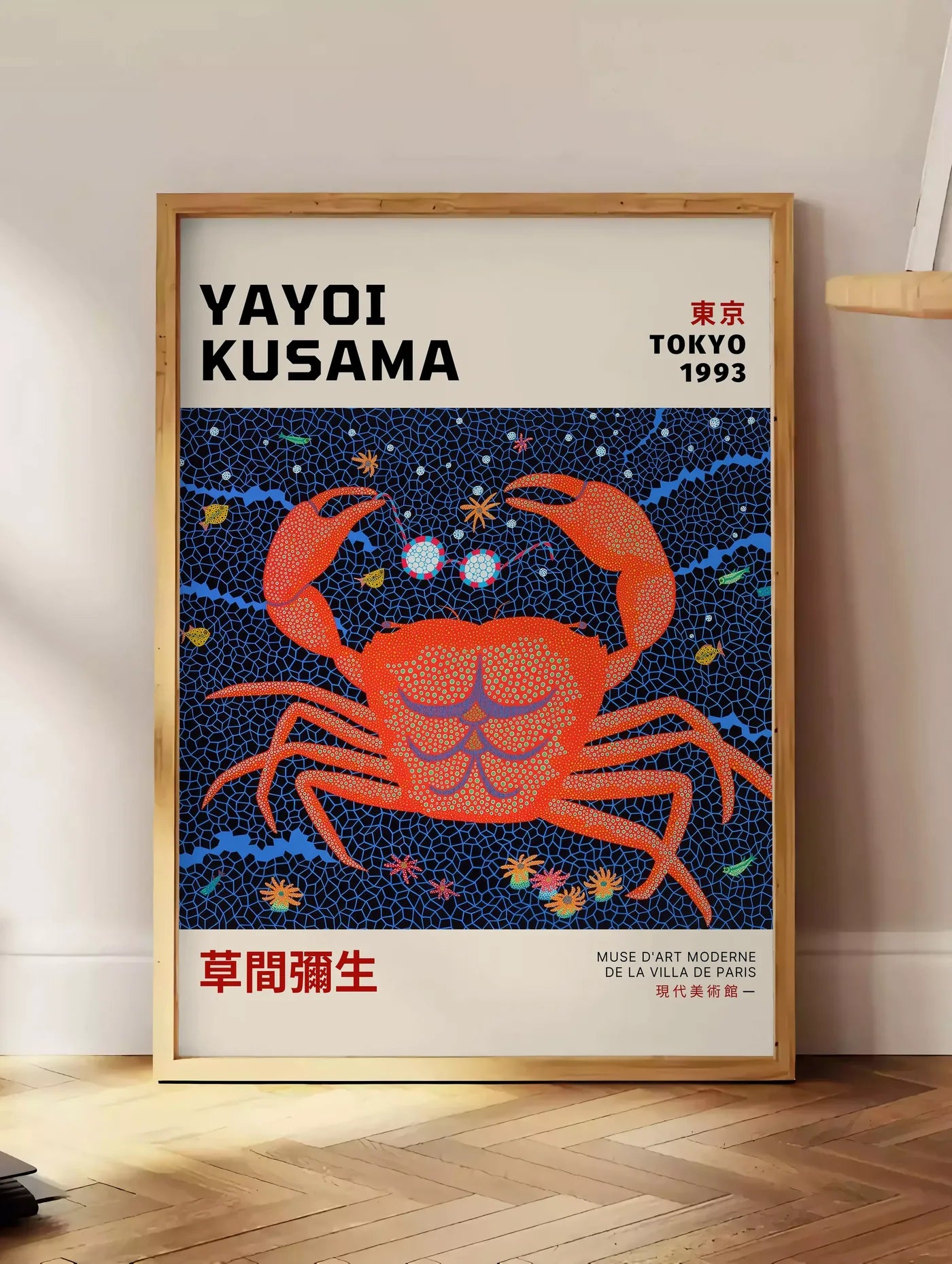 Estampe affiche crabe rouge a pois de Kusama art japonais, posee au sol dans un coin salon, sur un parquet a chevrons, pres d'une table d'appoint en chene chargee de livres