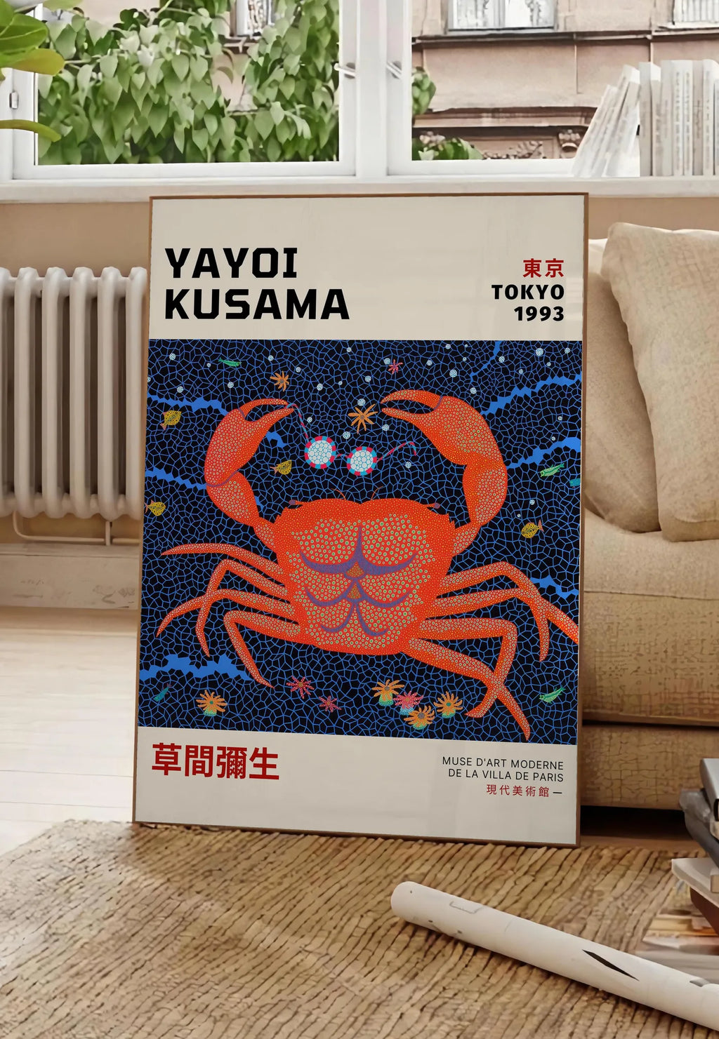 Poster affiche crabe rouge a pois de Kusama art japonais, posee au sol dans un salon parisien, devant une grande fenetre donnant sur un immeuble haussmannien, entre un ficus et un canape creme