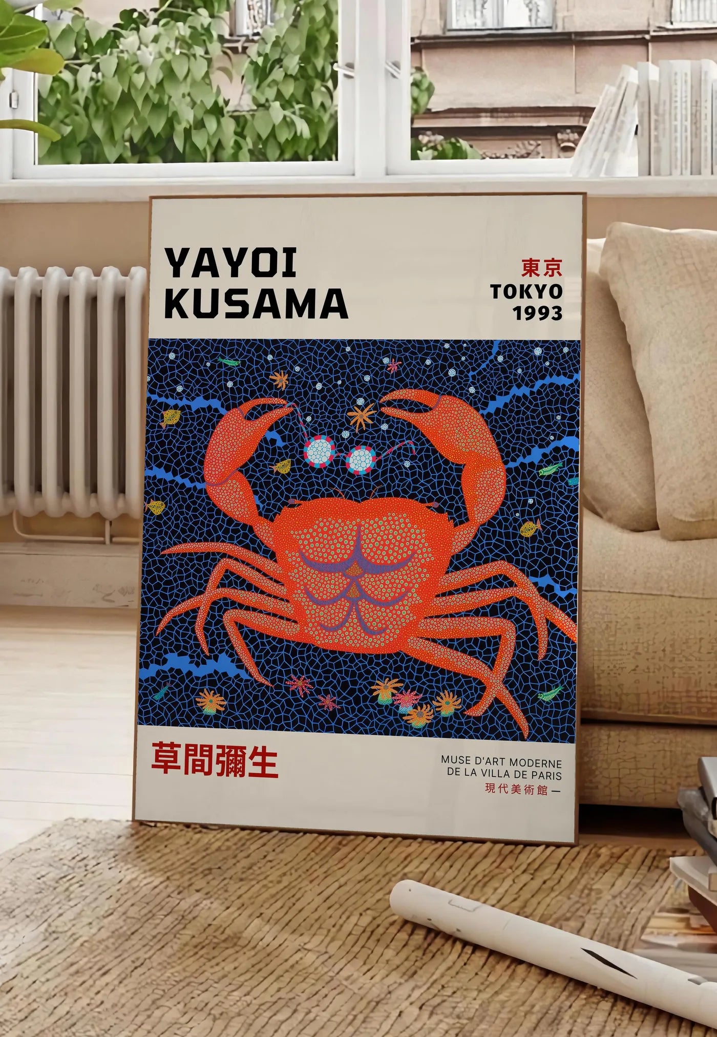 Poster affiche crabe rouge a pois de Kusama art japonais, posee au sol dans un salon parisien, devant une grande fenetre donnant sur un immeuble haussmannien, entre un ficus et un canape creme