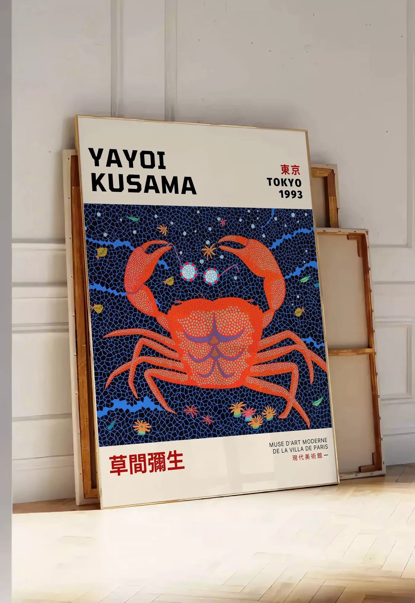 Tirage encadrable affiche crabe rouge a pois de Kusama art japonais, posee au sol dans une entree lumineuse, contre un mur a panneaux blancs, a cote de chassis en bois empiles