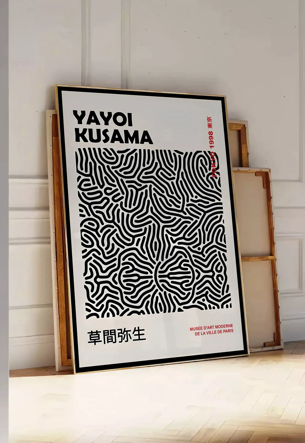 Tirage encadrable affiche filet infini de Kusama art japonais, posee au sol dans une entree lumineuse, contre un mur a panneaux blancs, a cote de chassis en bois empiles