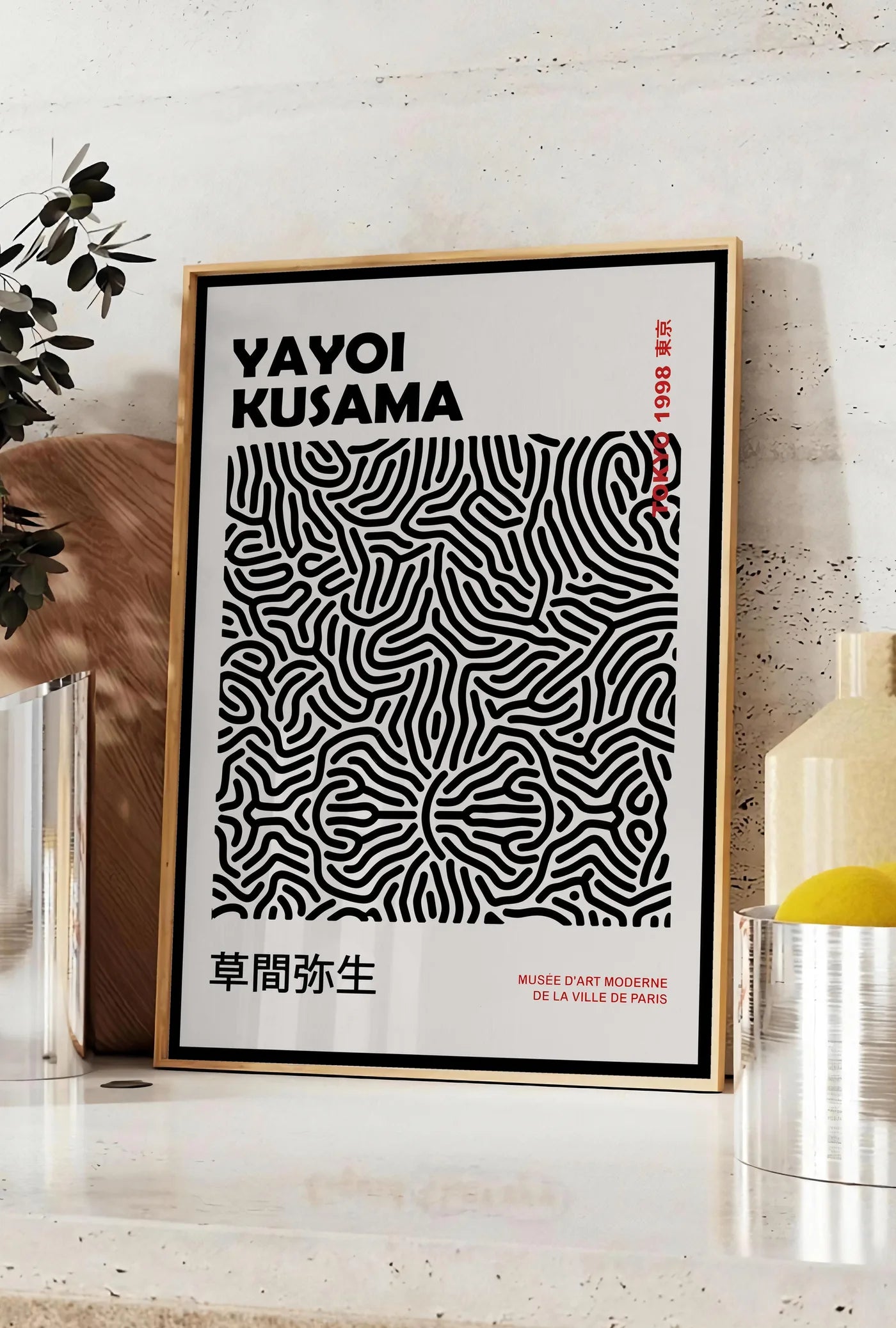 Affiche affiche filet infini noir de Kusama art japonais, posee sur un plan de travail de cuisine en pierre claire, entre une branche d'eucalyptus en vase et un bocal de citrons