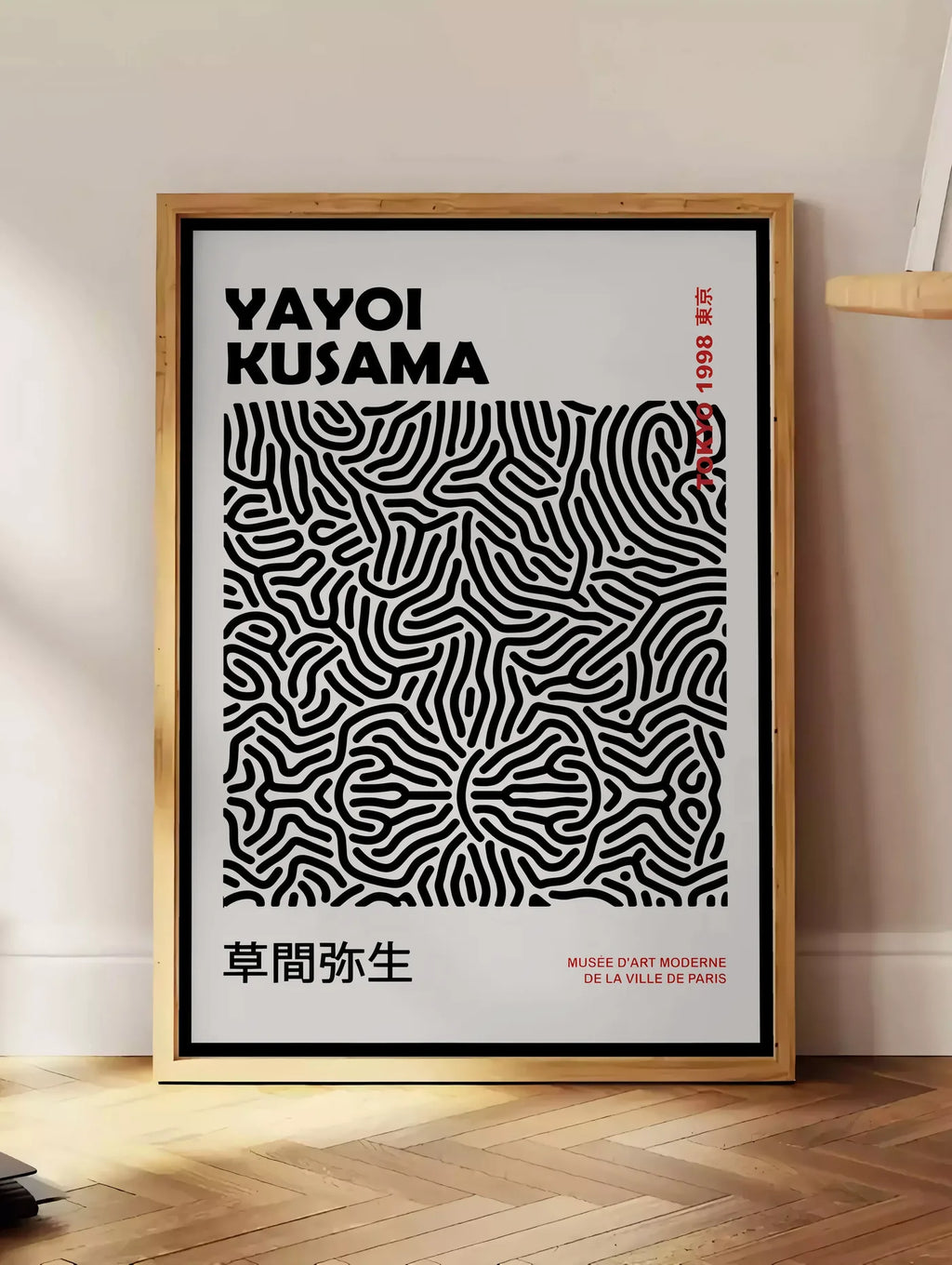 Estampe affiche filet infini noir de Kusama art japonais, posee au sol dans un coin salon, sur un parquet a chevrons, pres d'une table d'appoint en chene chargee de livres
