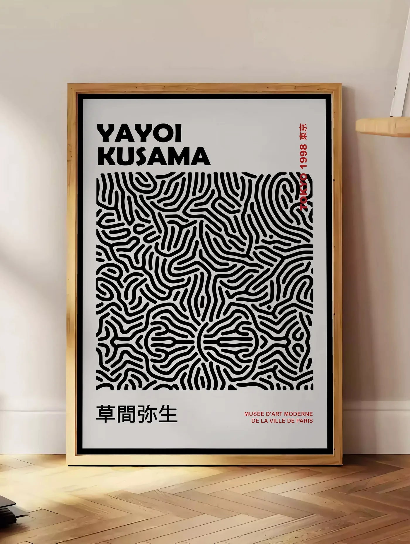 Estampe affiche filet infini noir de Kusama art japonais, posee au sol dans un coin salon, sur un parquet a chevrons, pres d'une table d'appoint en chene chargee de livres