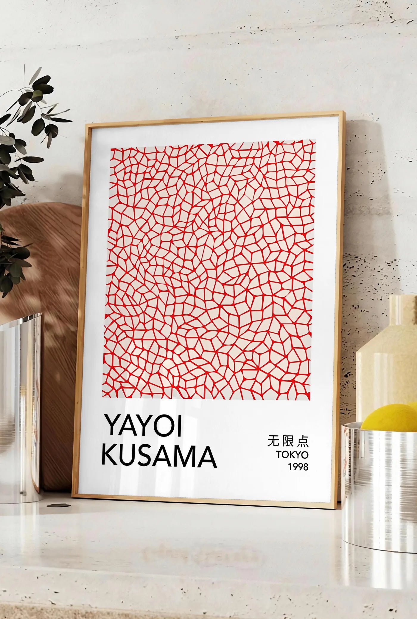 Affiche affiche filet infini rouge de Kusama art japonais, posee sur un plan de travail de cuisine en pierre claire, entre une branche d'eucalyptus en vase et un bocal de citrons