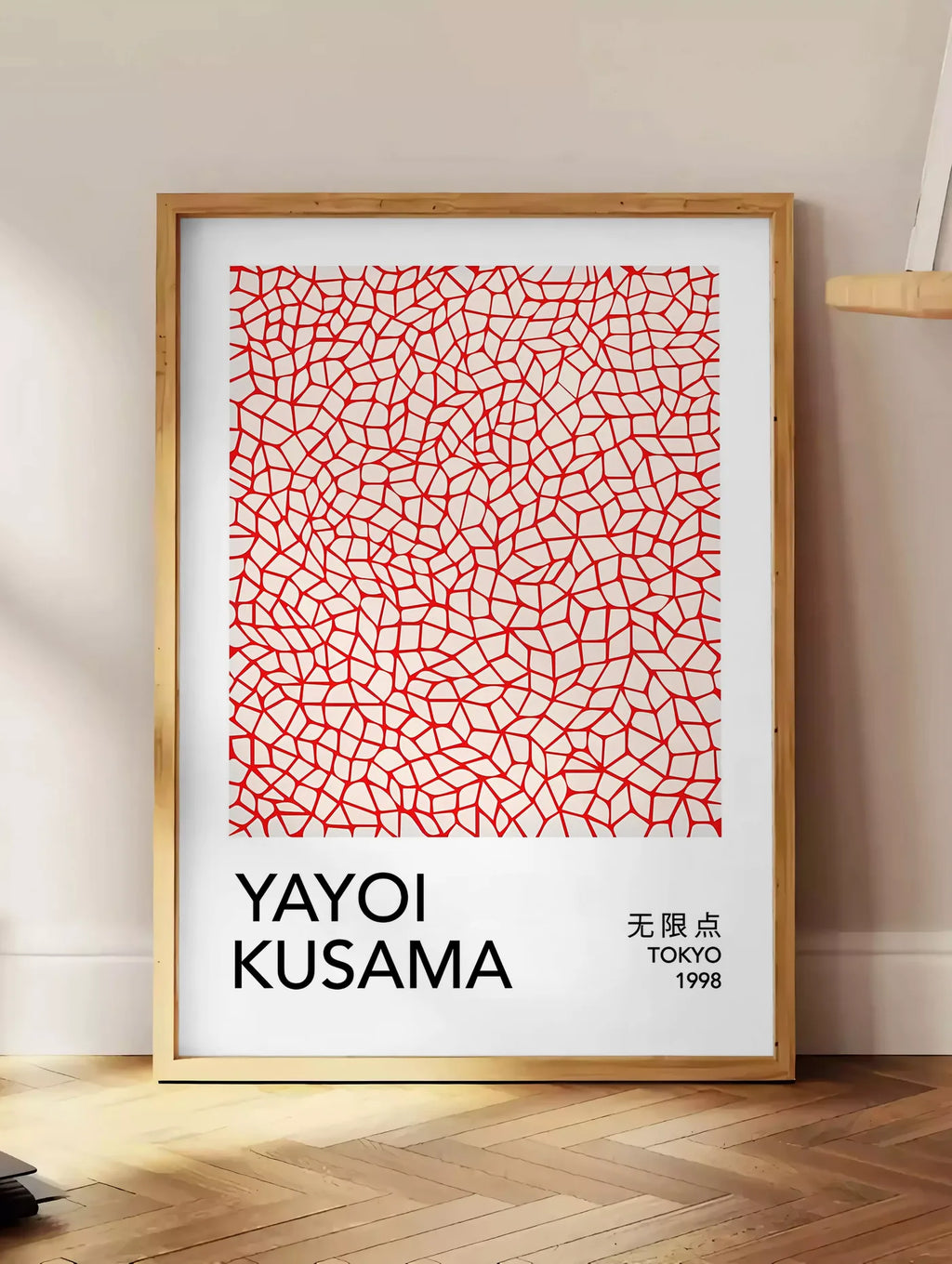 Estampe affiche filet infini rouge de Kusama art japonais, posee au sol dans un coin salon, sur un parquet a chevrons, pres d'une table d'appoint en chene chargee de livres