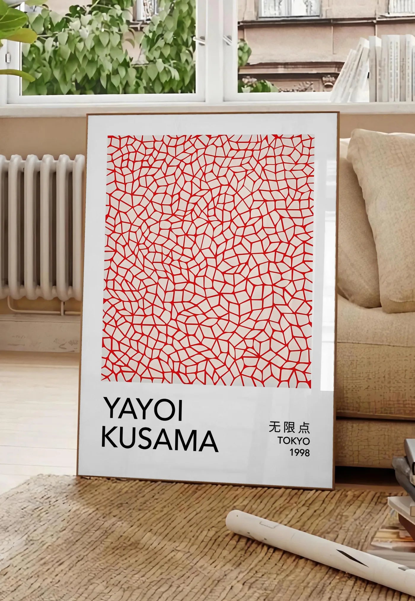 Poster affiche filet infini rouge de Kusama art japonais, posee au sol dans un salon parisien, devant une grande fenetre donnant sur un immeuble haussmannien, entre un ficus et un canape creme