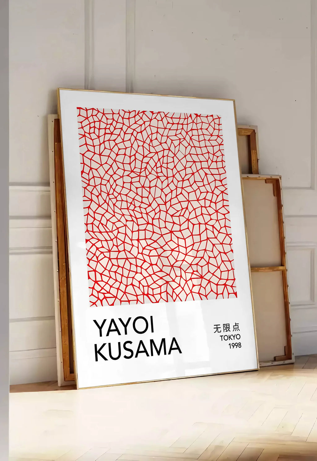 Tirage encadrable affiche filet infini rouge de Kusama art japonais, posee au sol dans une entree lumineuse, contre un mur a panneaux blancs, a cote de chassis en bois empiles