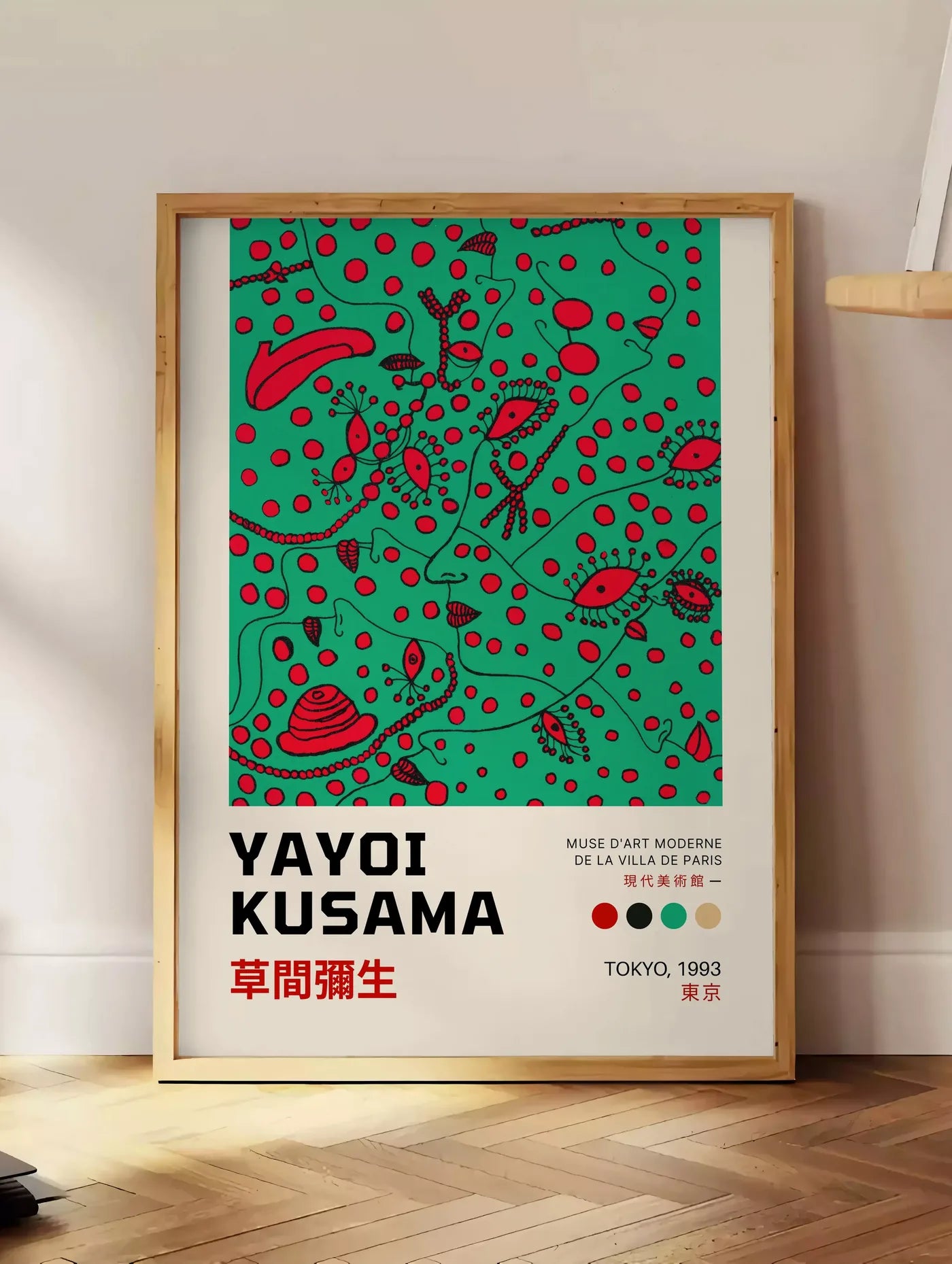 Estampe affiche formes rouges de Kusama art japonais, posee au sol dans un coin salon, sur un parquet a chevrons, pres d'une table d'appoint en chene chargee de livres