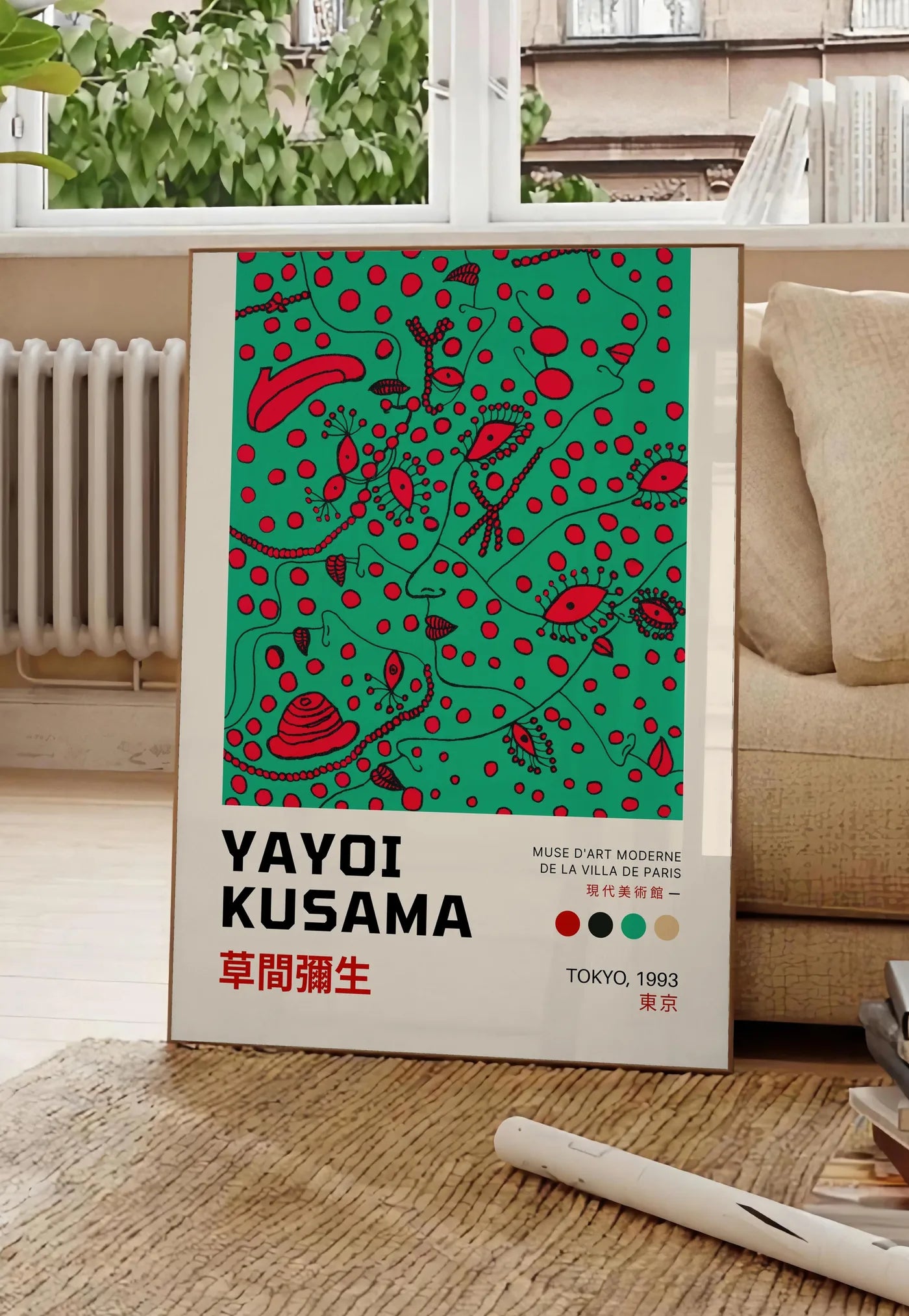 Poster affiche formes rouges de Kusama art japonais, posee au sol dans un salon parisien, devant une grande fenetre donnant sur un immeuble haussmannien, entre un ficus et un canape creme