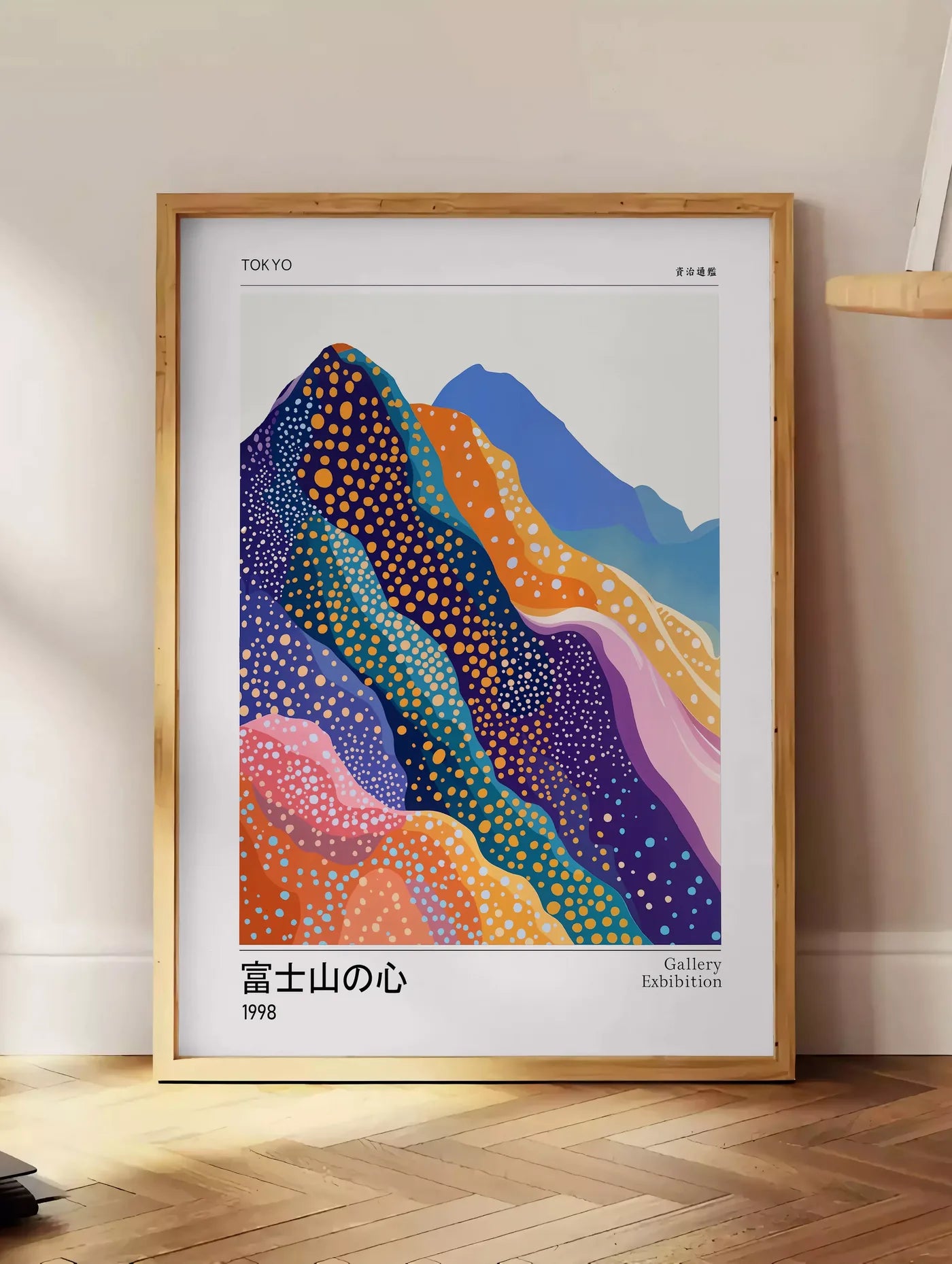 Estampe affiche montagnes Fuji de Kusama art japonais, posee au sol dans un coin salon, sur un parquet a chevrons, pres d'une table d'appoint en chene chargee de livres