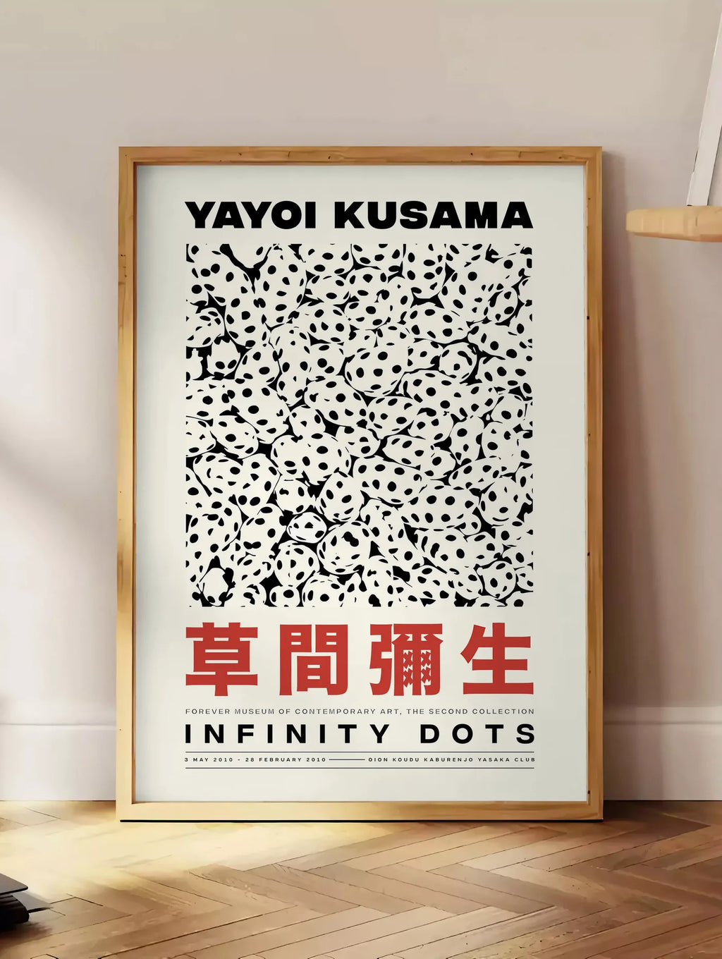 Estampe affiche pois noir et blanc de Kusama art japonais, posee au sol dans un coin salon, sur un parquet a chevrons, pres d'une table d'appoint en chene chargee de livres