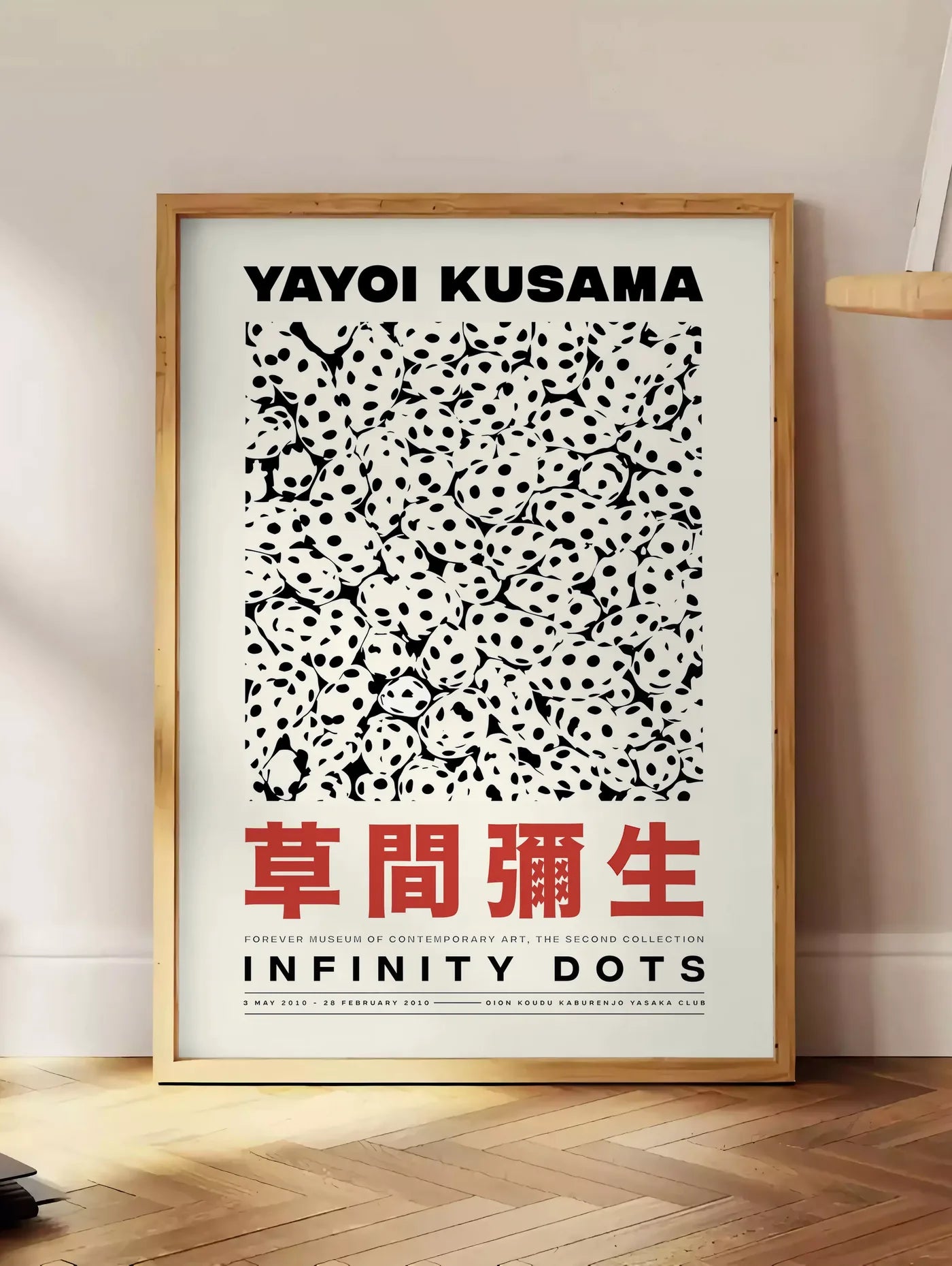 Estampe affiche pois noir et blanc de Kusama art japonais, posee au sol dans un coin salon, sur un parquet a chevrons, pres d'une table d'appoint en chene chargee de livres