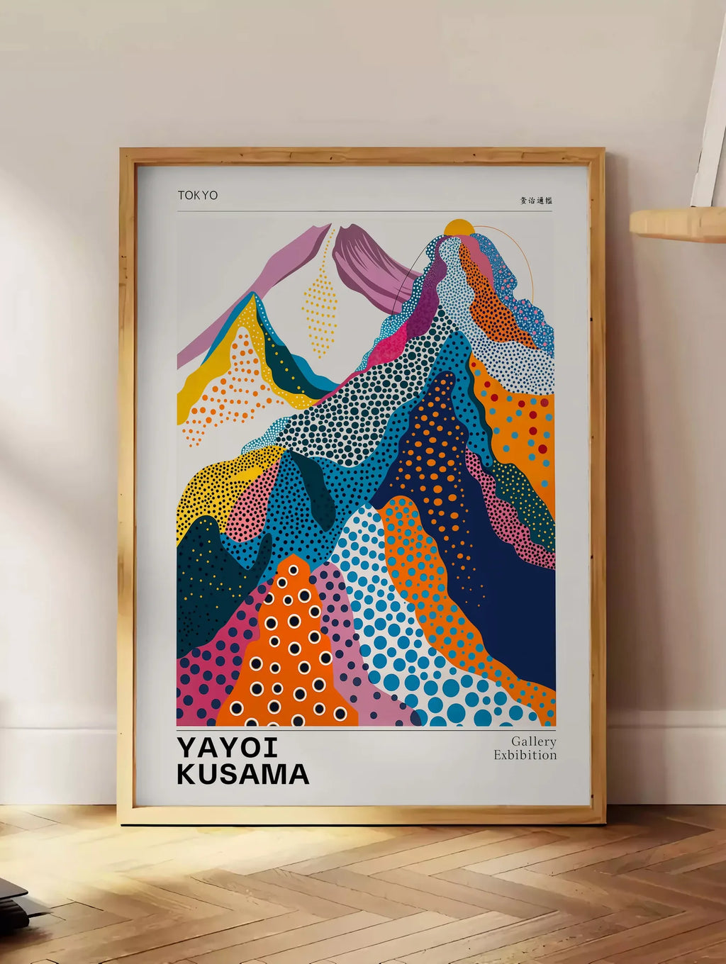 Estampe affiche montagnes multicolores de Kusama art japonais, posee au sol dans un coin salon, sur un parquet a chevrons, pres d'une table d'appoint en chene chargee de livres