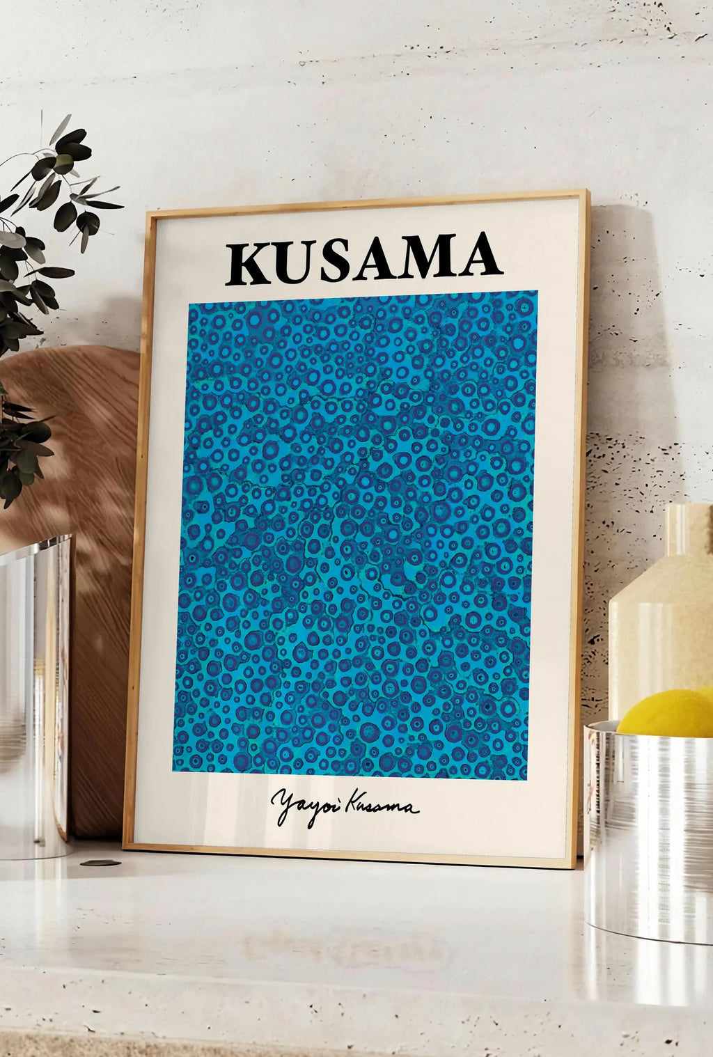 Affiche affiche pois bleus de Kusama art japonais, posee sur un plan de travail de cuisine en pierre claire, entre une branche d'eucalyptus en vase et un bocal de citrons
