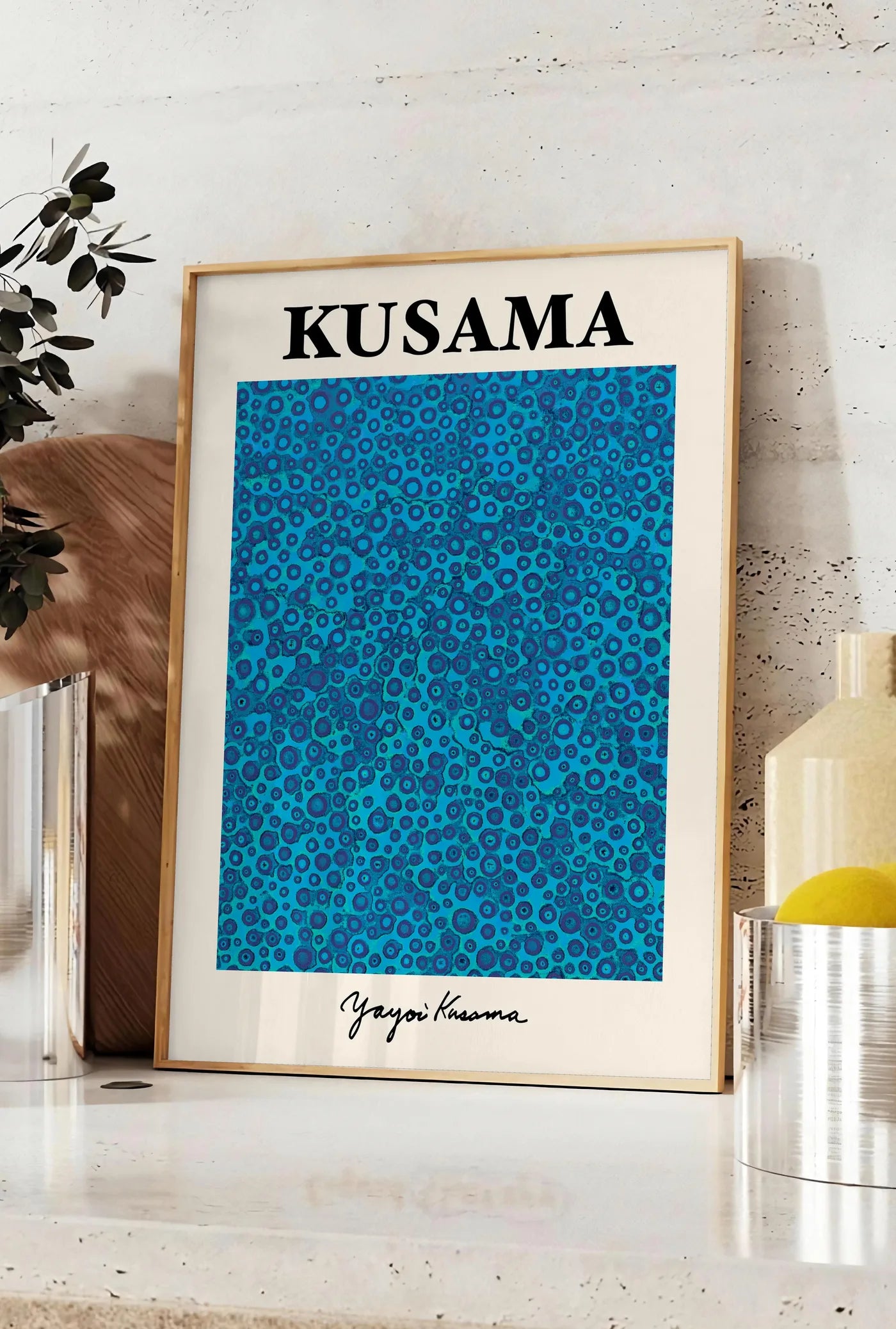 Affiche affiche pois bleus de Kusama art japonais, posee sur un plan de travail de cuisine en pierre claire, entre une branche d'eucalyptus en vase et un bocal de citrons