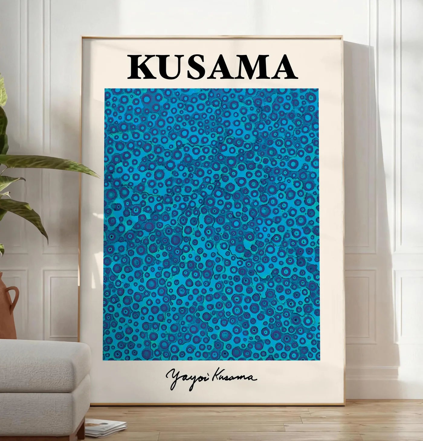 Reproduction affiche pois bleus de Kusama art japonais, posee au sol dans un salon minimaliste clair, a cote d'un canape beige et d'une plante verte, sur un parquet clair