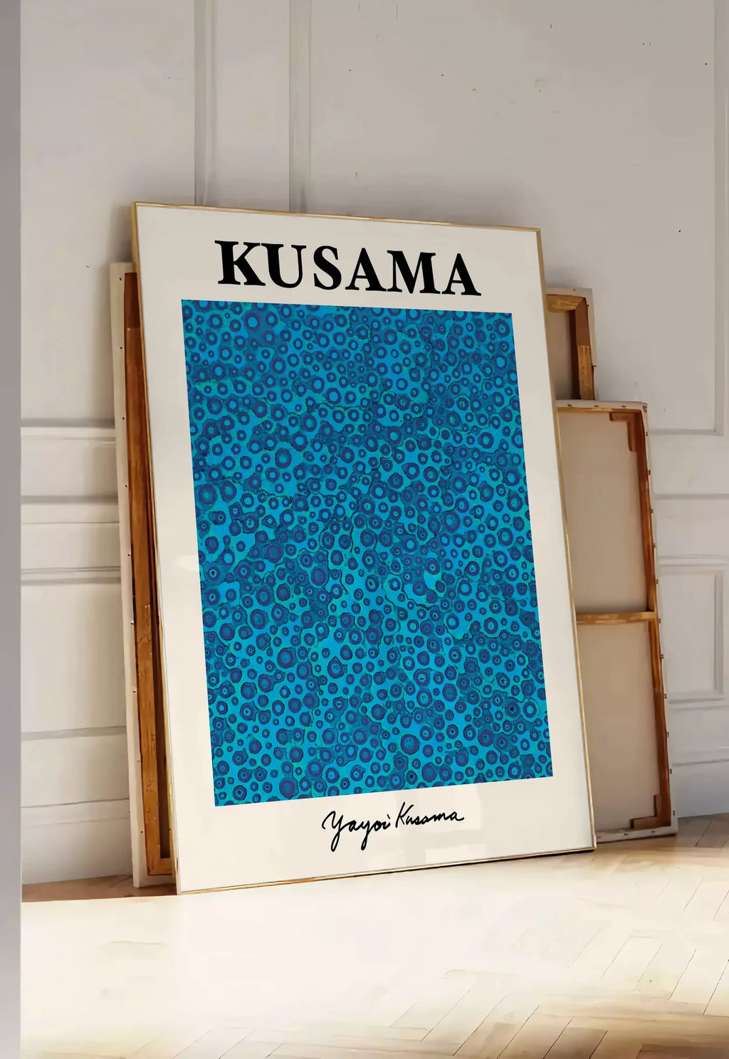 Tirage encadrable affiche pois bleus de Kusama art japonais, posee au sol dans une entree lumineuse, contre un mur a panneaux blancs, a cote de chassis en bois empiles