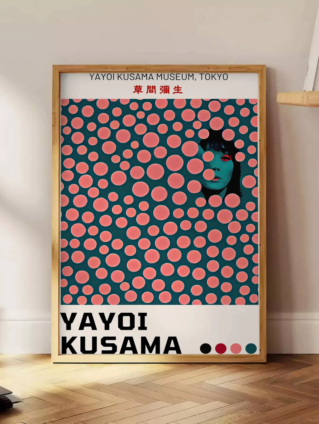 Estampe affiche pois corail de Kusama art japonais, posee au sol dans un coin salon, sur un parquet a chevrons, pres d'une table d'appoint en chene chargee de livres