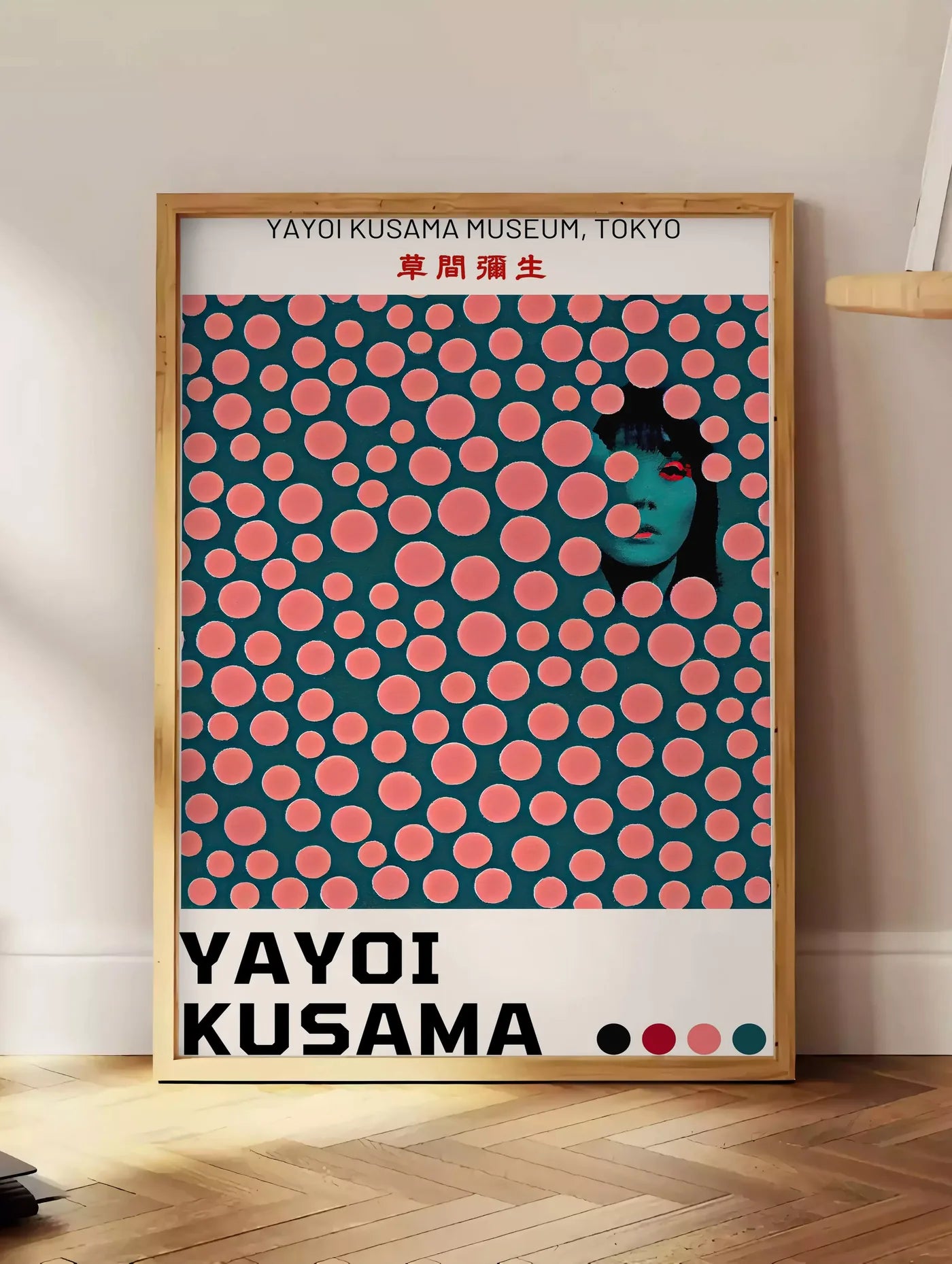 Estampe affiche pois corail de Kusama art japonais, posee au sol dans un coin salon, sur un parquet a chevrons, pres d'une table d'appoint en chene chargee de livres