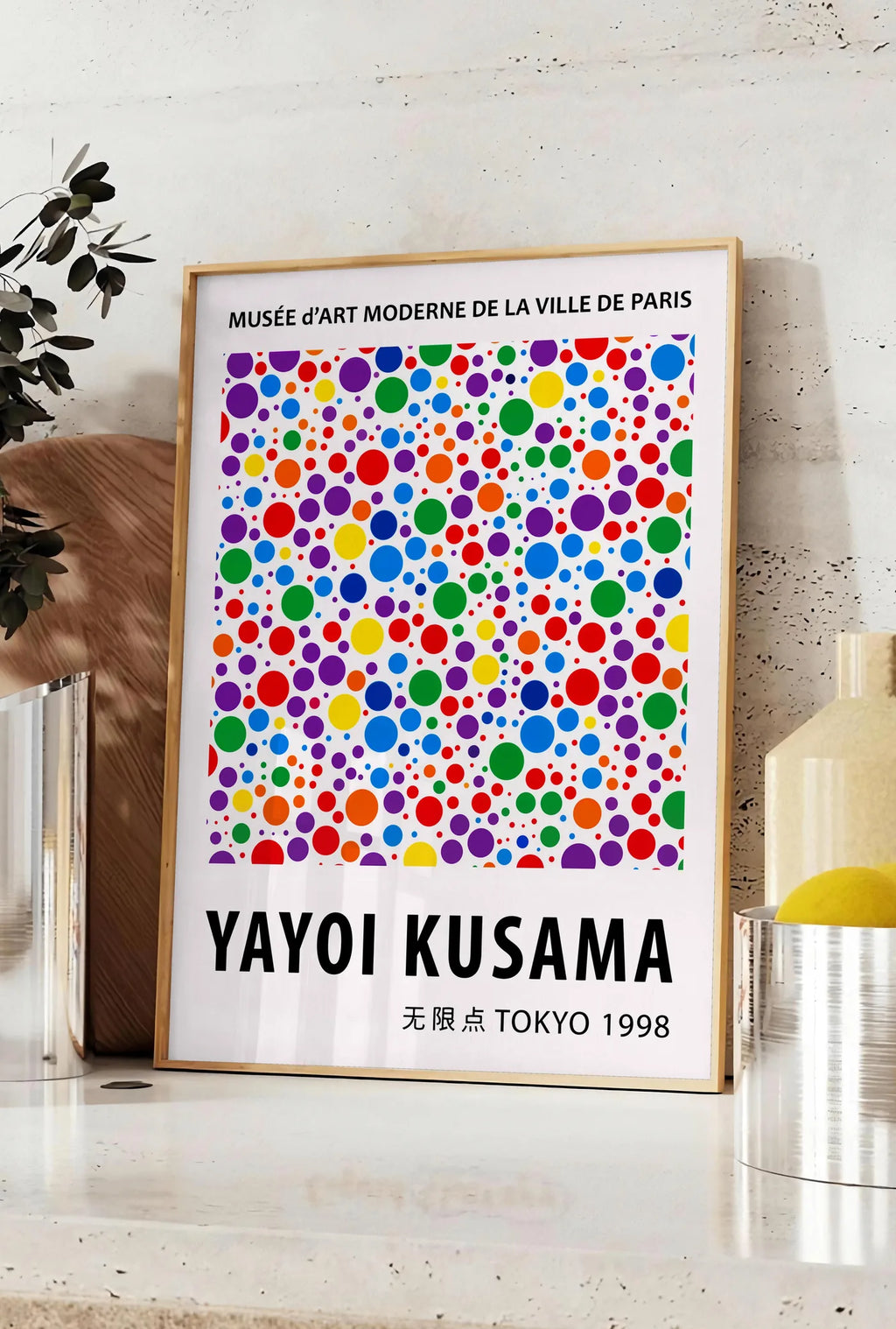 Affiche affiche pois multicolores de Kusama art japonais, posee sur un plan de travail de cuisine en pierre claire, entre une branche d'eucalyptus en vase et un bocal de citrons