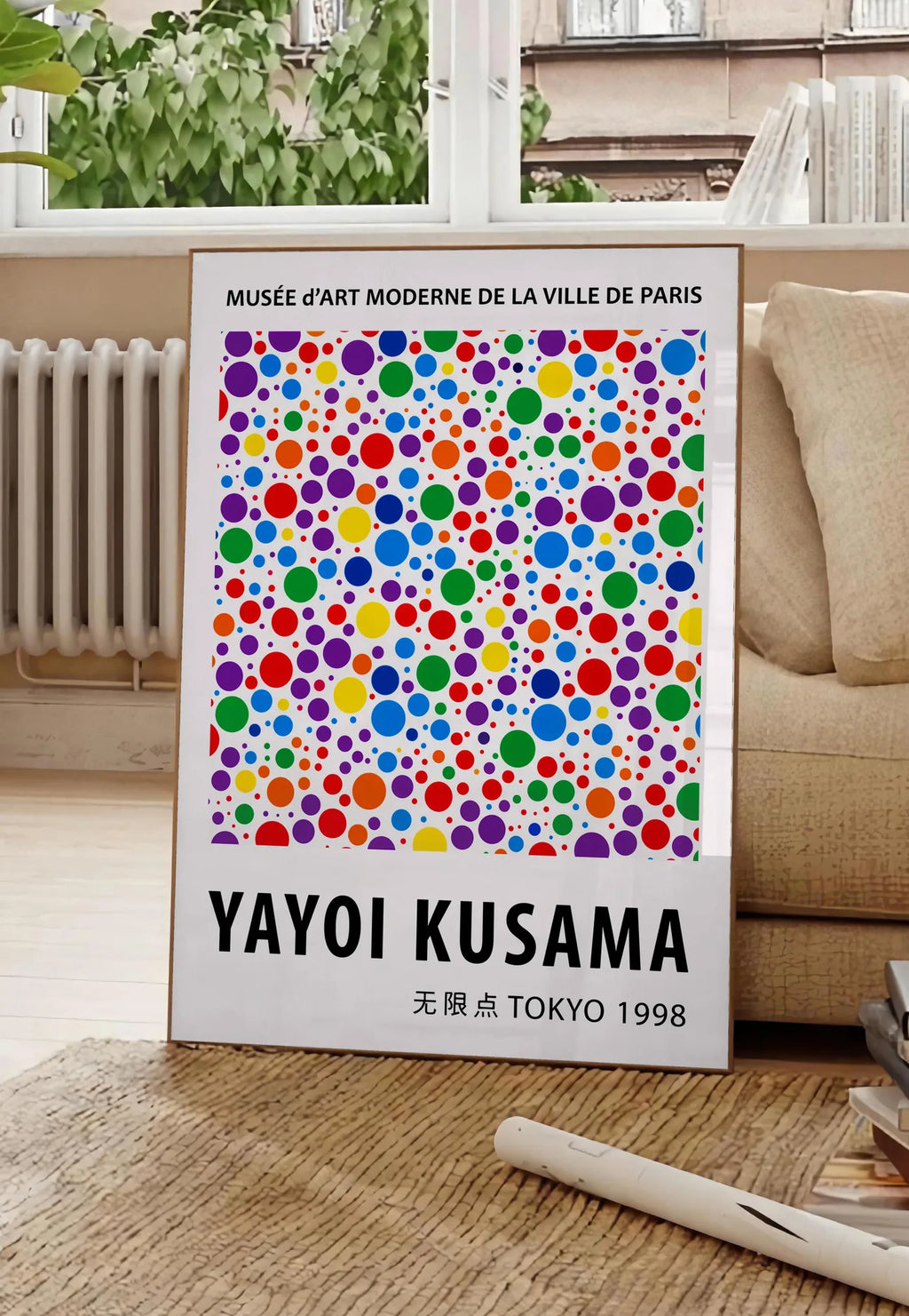 Poster affiche pois multicolores de Kusama art japonais, posee au sol dans un salon parisien, devant une grande fenetre donnant sur un immeuble haussmannien, entre un ficus et un canape creme