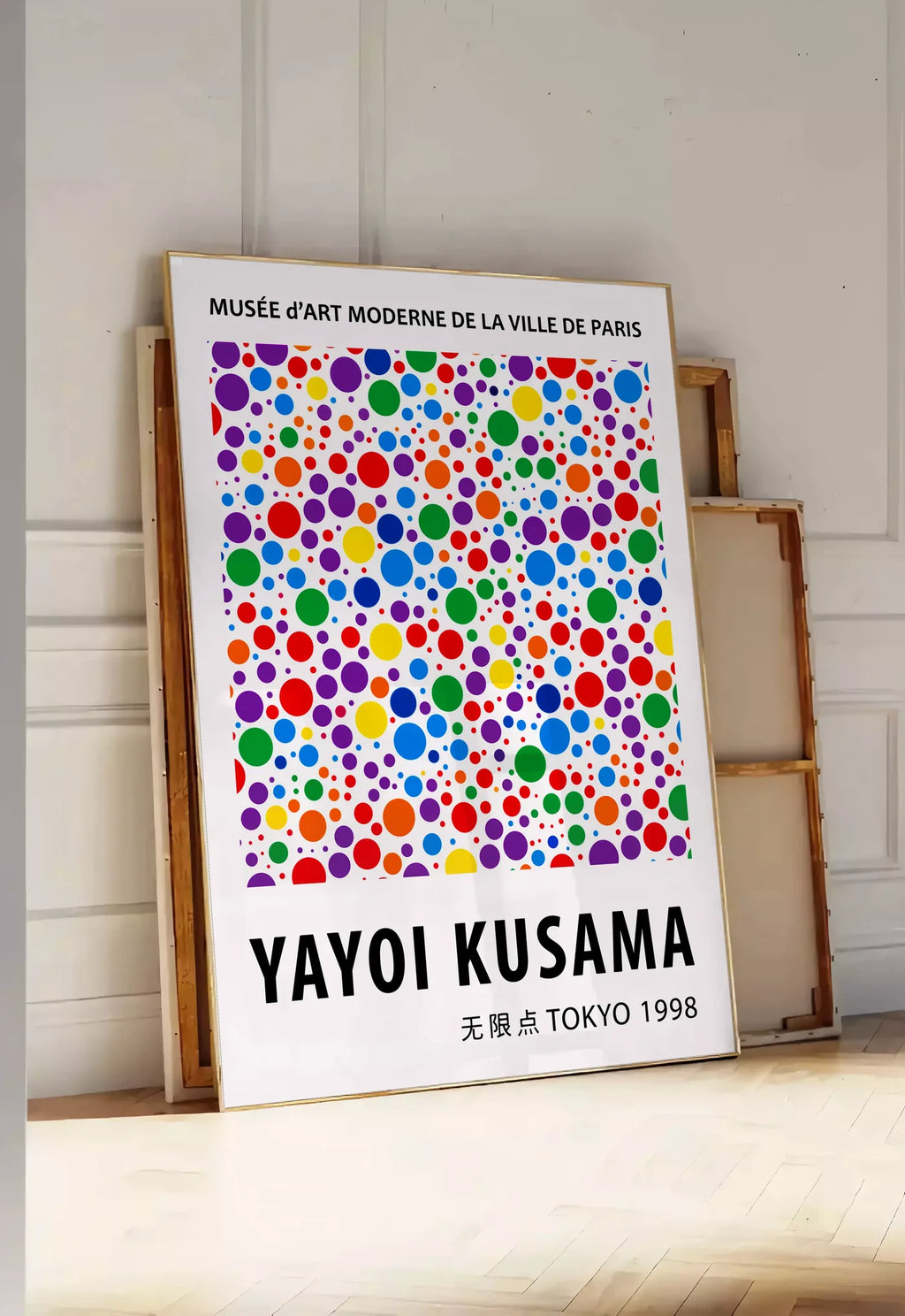 Tirage encadrable affiche pois multicolores de Kusama art japonais, posee au sol dans une entree lumineuse, contre un mur a panneaux blancs, a cote de chassis en bois empiles