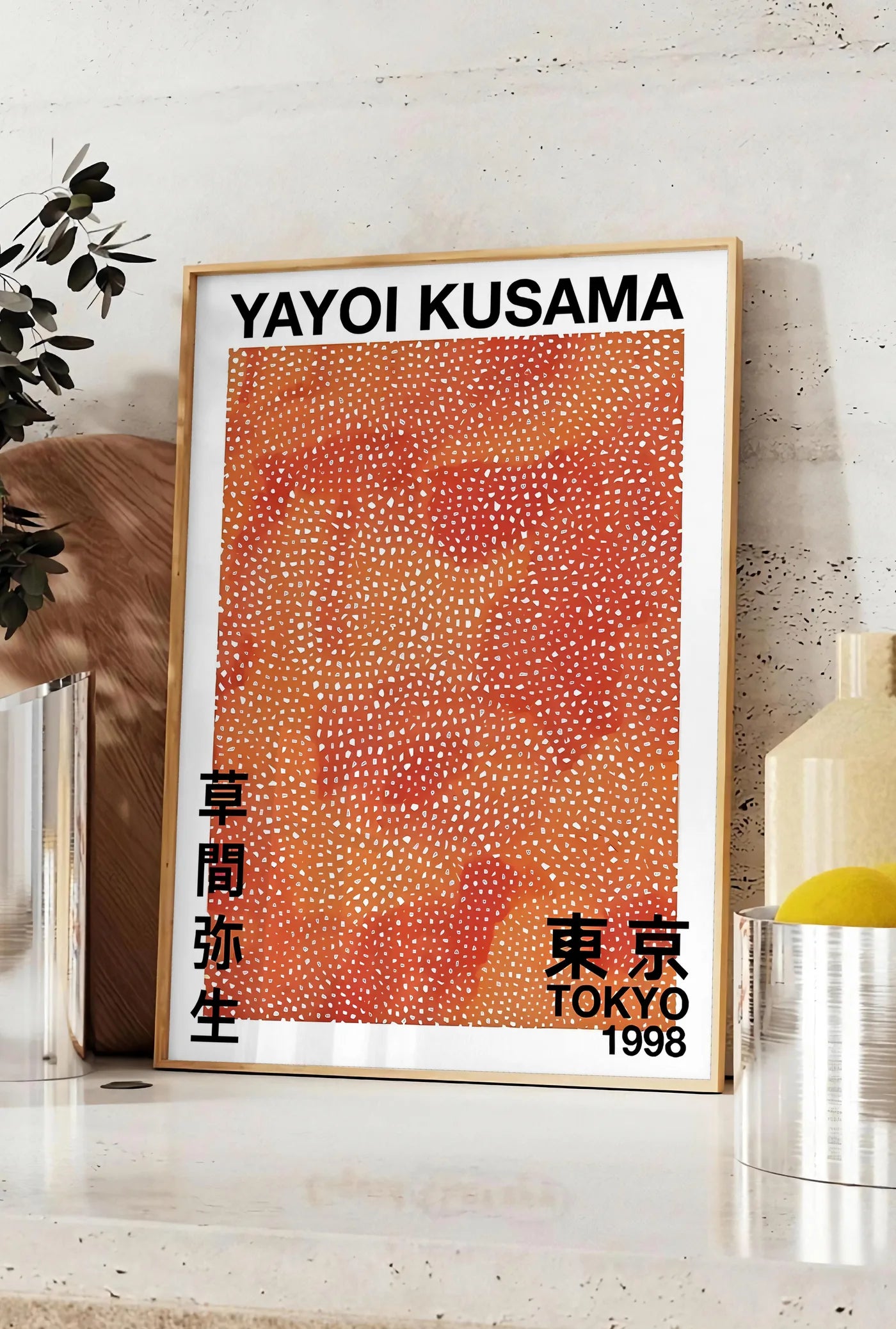 Affiche affiche pois orange de Kusama art japonais, posee sur un plan de travail de cuisine en pierre claire, entre une branche d'eucalyptus en vase et un bocal de citrons