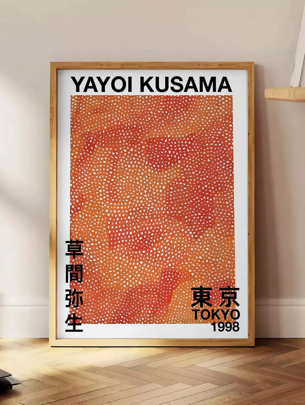 Estampe affiche pois orange de Kusama art japonais, posee au sol dans un coin salon, sur un parquet a chevrons, pres d'une table d'appoint en chene chargee de livres