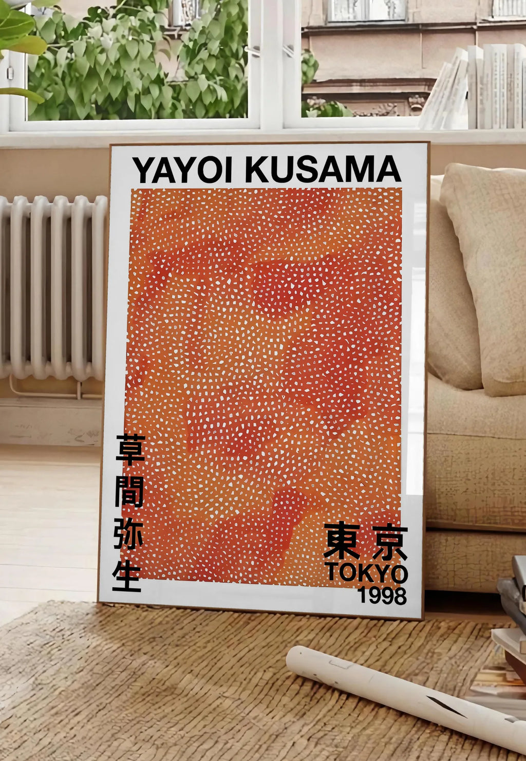 Poster affiche pois orange de Kusama art japonais, posee au sol dans un salon parisien, devant une grande fenetre donnant sur un immeuble haussmannien, entre un ficus et un canape creme