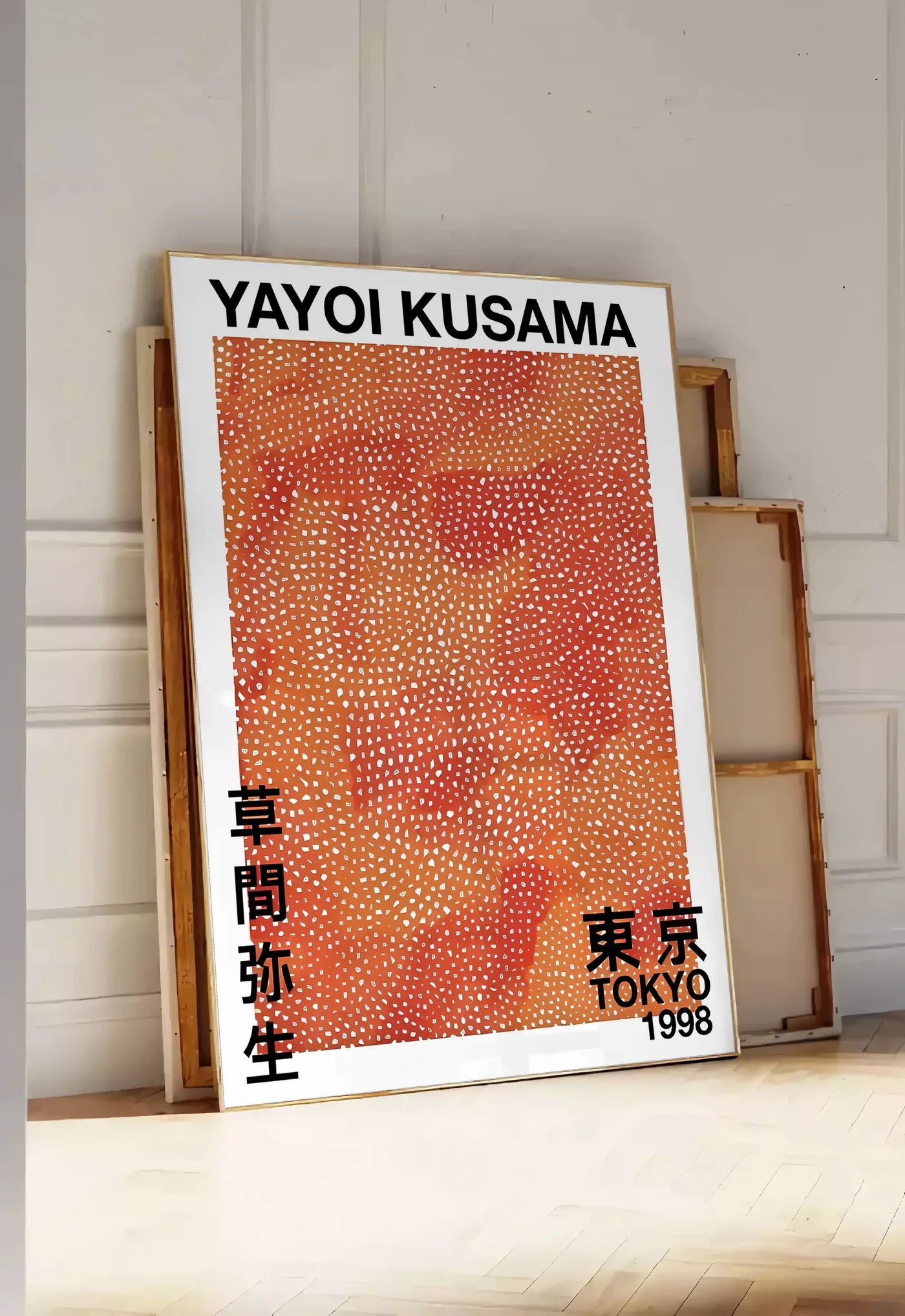 Tirage encadrable affiche pois orange de Kusama art japonais, posee au sol dans une entree lumineuse, contre un mur a panneaux blancs, a cote de chassis en bois empiles