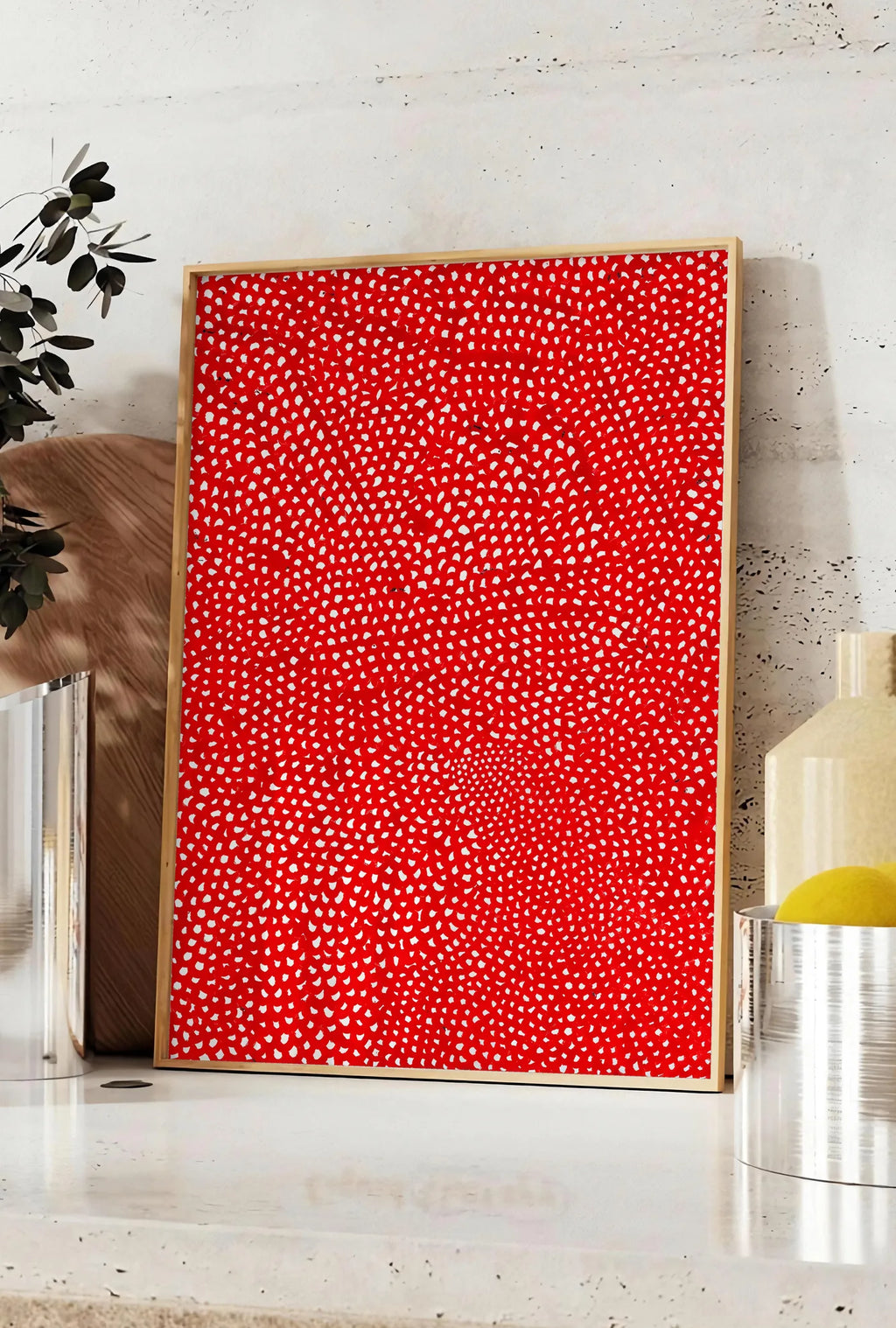 Affiche affiche pois rouge et blanc de Kusama art japonais, posee sur un plan de travail de cuisine en pierre claire, entre une branche d'eucalyptus en vase et un bocal de citrons