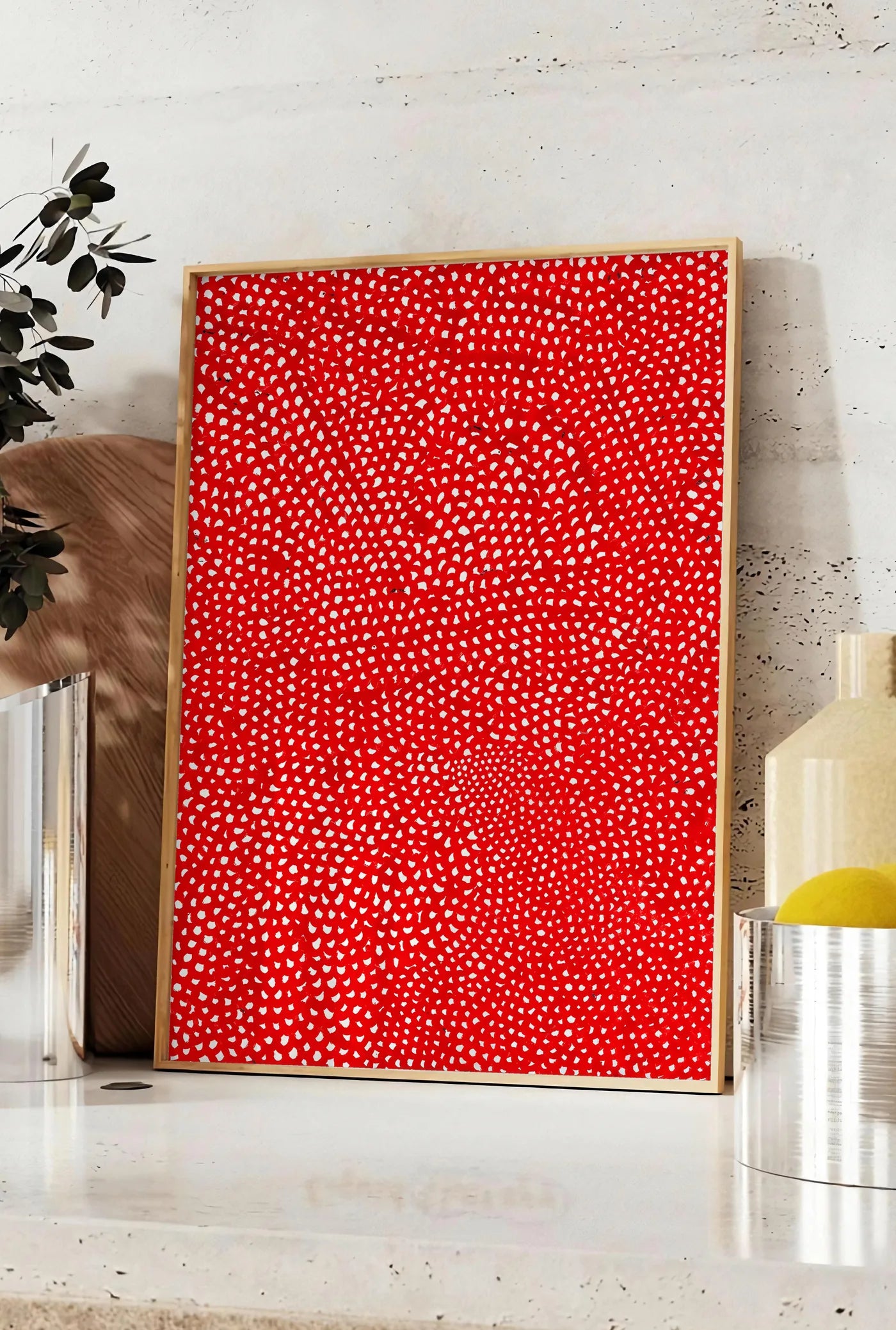 Affiche affiche pois rouge et blanc de Kusama art japonais, posee sur un plan de travail de cuisine en pierre claire, entre une branche d'eucalyptus en vase et un bocal de citrons