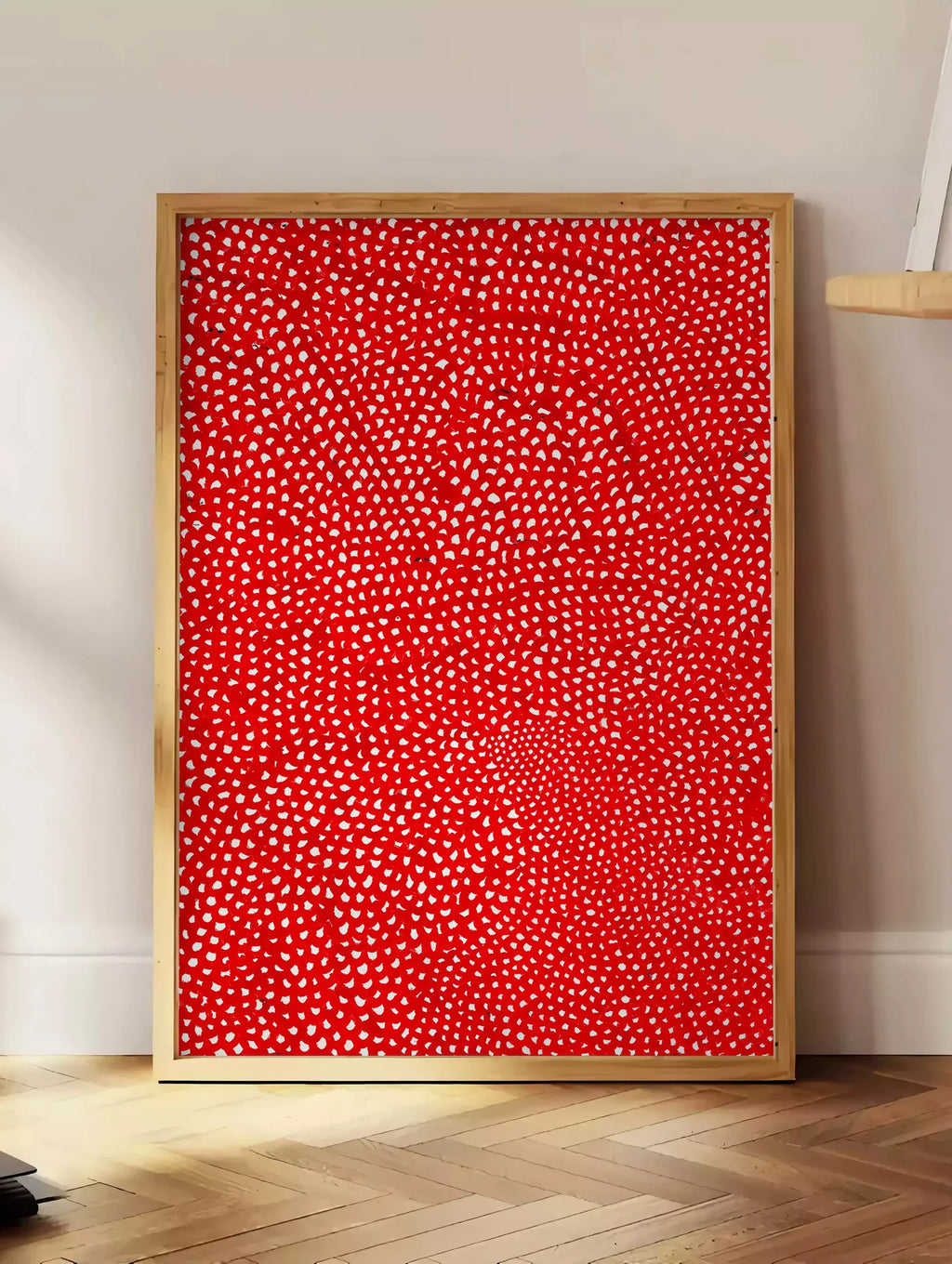 Estampe affiche pois rouge et blanc de Kusama art japonais, posee au sol dans un coin salon, sur un parquet a chevrons, pres d'une table d'appoint en chene chargee de livres