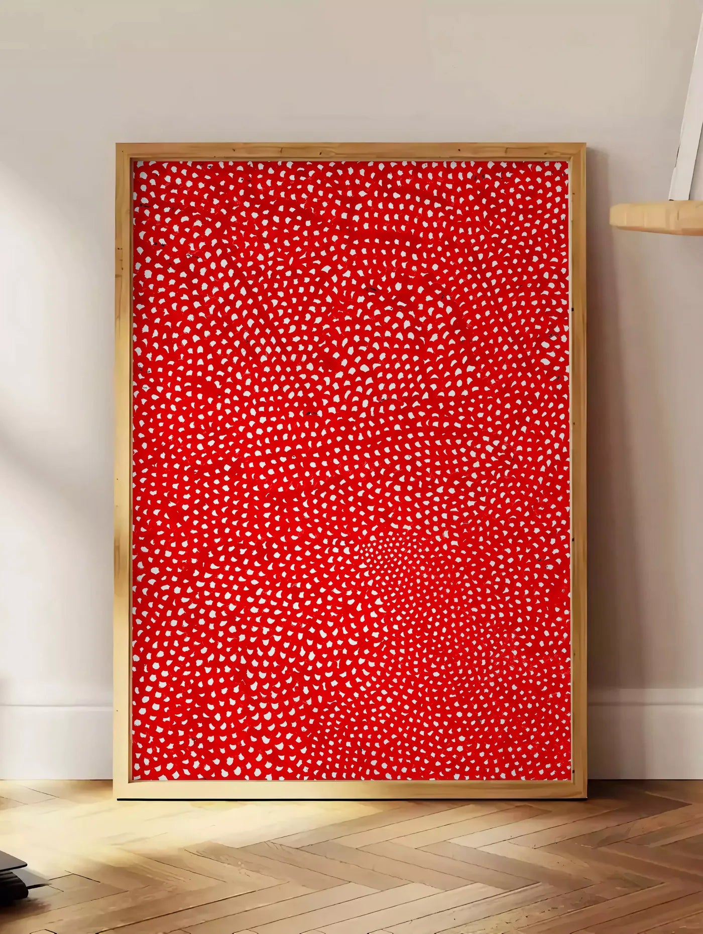 Estampe affiche pois rouge et blanc de Kusama art japonais, posee au sol dans un coin salon, sur un parquet a chevrons, pres d'une table d'appoint en chene chargee de livres