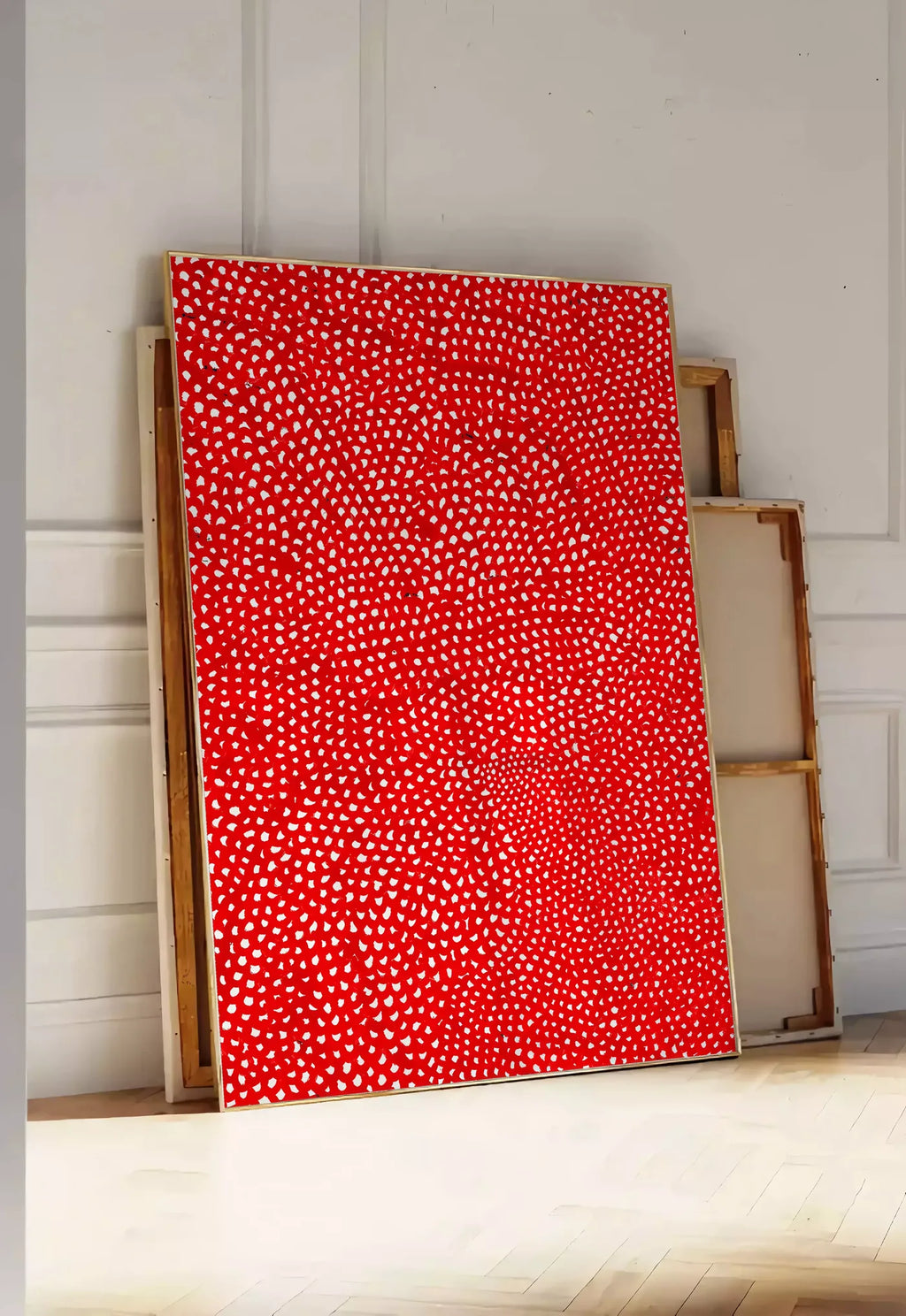 Tirage encadrable affiche pois rouge et blanc de Kusama art japonais, posee au sol dans une entree lumineuse, contre un mur a panneaux blancs, a cote de chassis en bois empiles