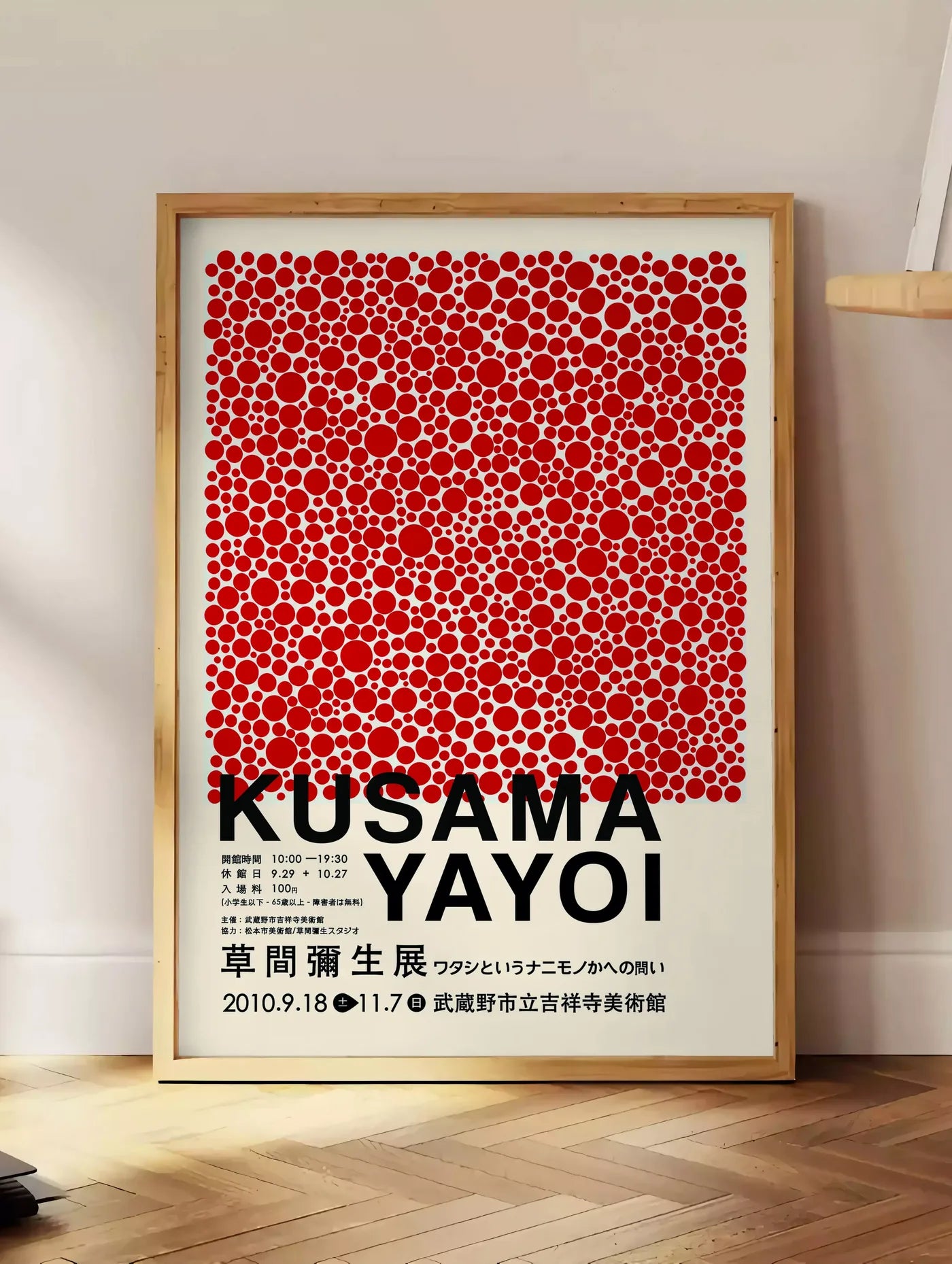 Estampe affiche pois rouges de Kusama art japonais, posee au sol dans un coin salon, sur un parquet a chevrons, pres d'une table d'appoint en chene chargee de livres