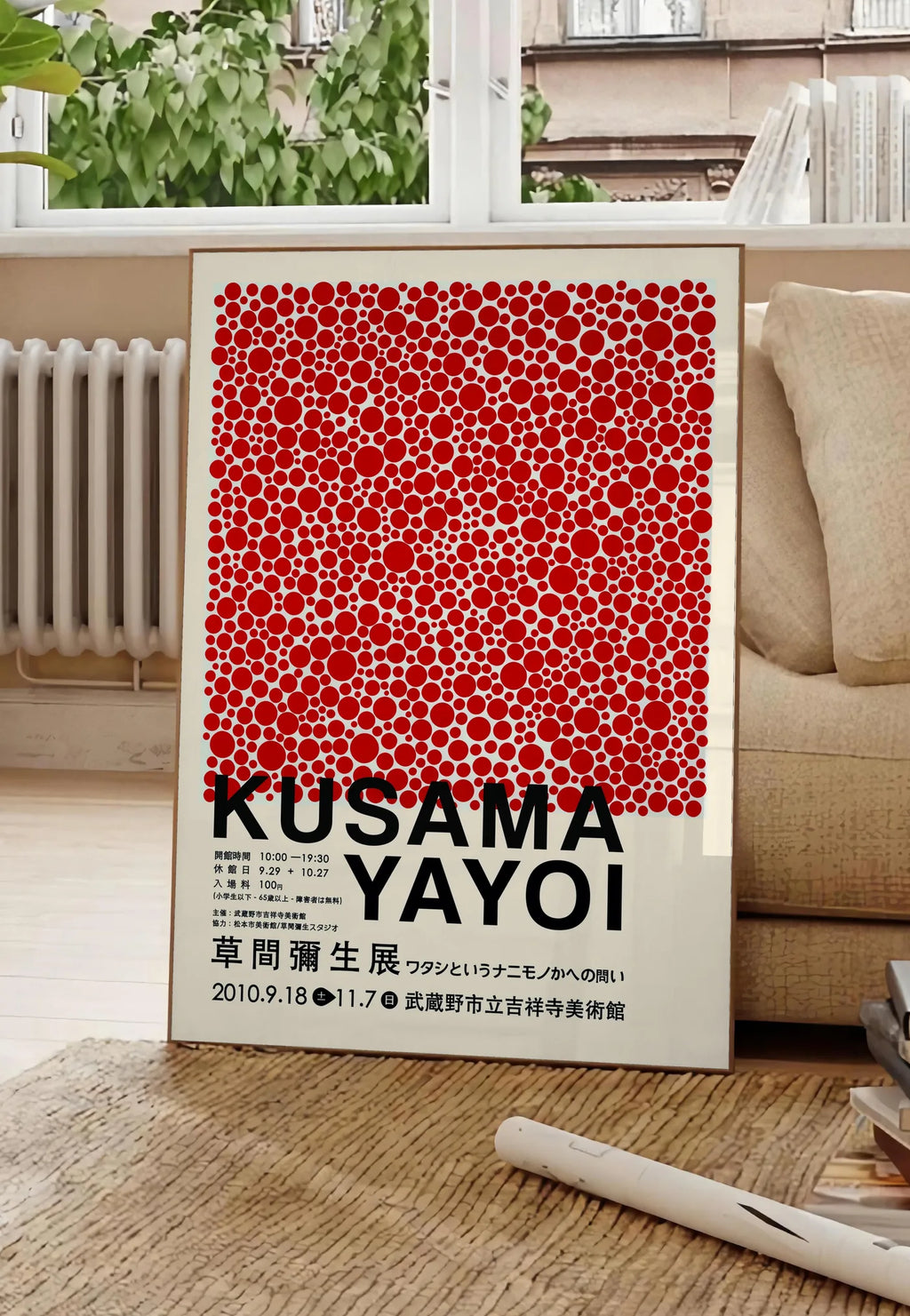 Poster affiche pois rouges de Kusama art japonais, posee au sol dans un salon parisien, devant une grande fenetre donnant sur un immeuble haussmannien, entre un ficus et un canape creme