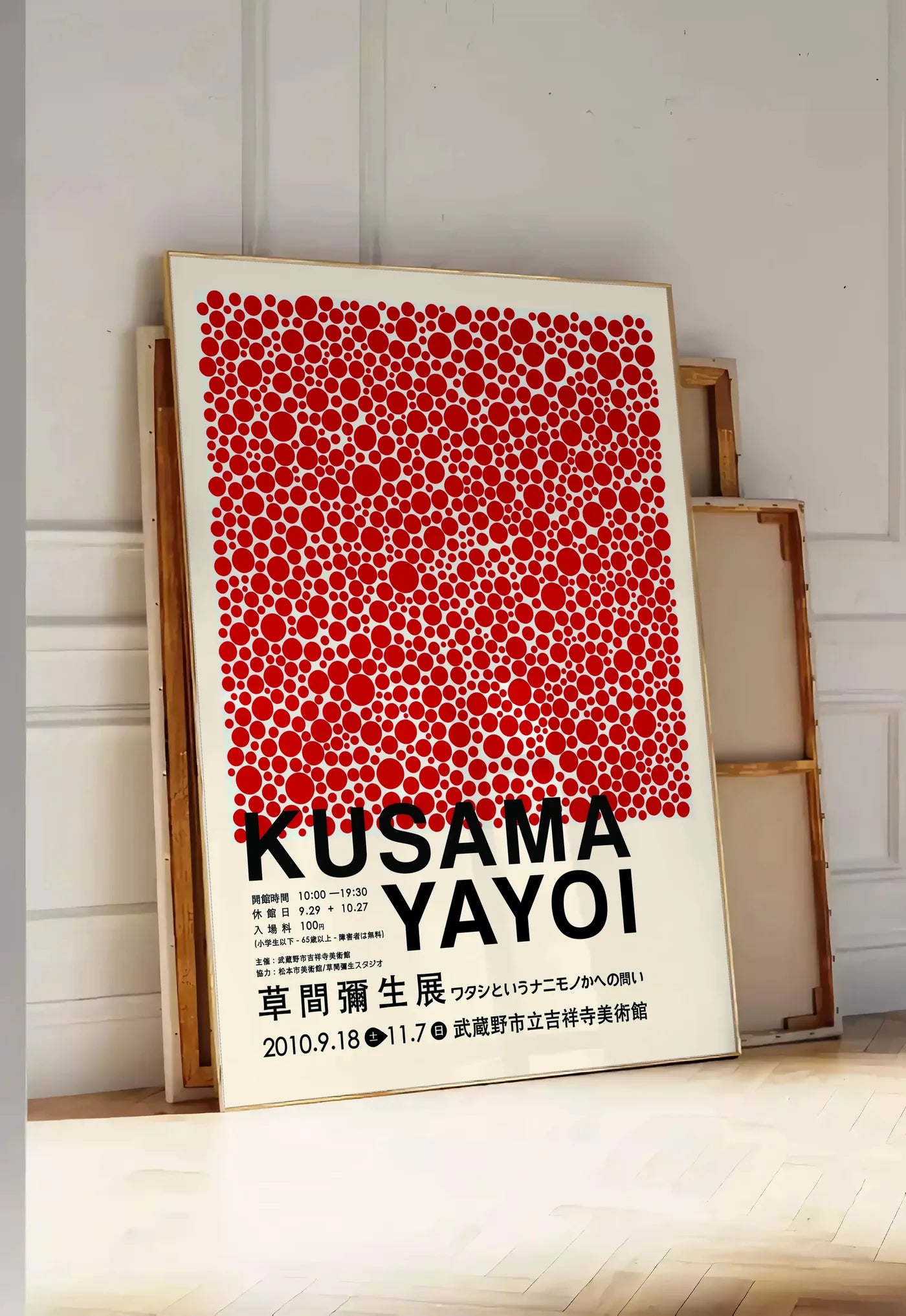 Tirage encadrable affiche pois rouges de Kusama art japonais, posee au sol dans une entree lumineuse, contre un mur a panneaux blancs, a cote de chassis en bois empiles